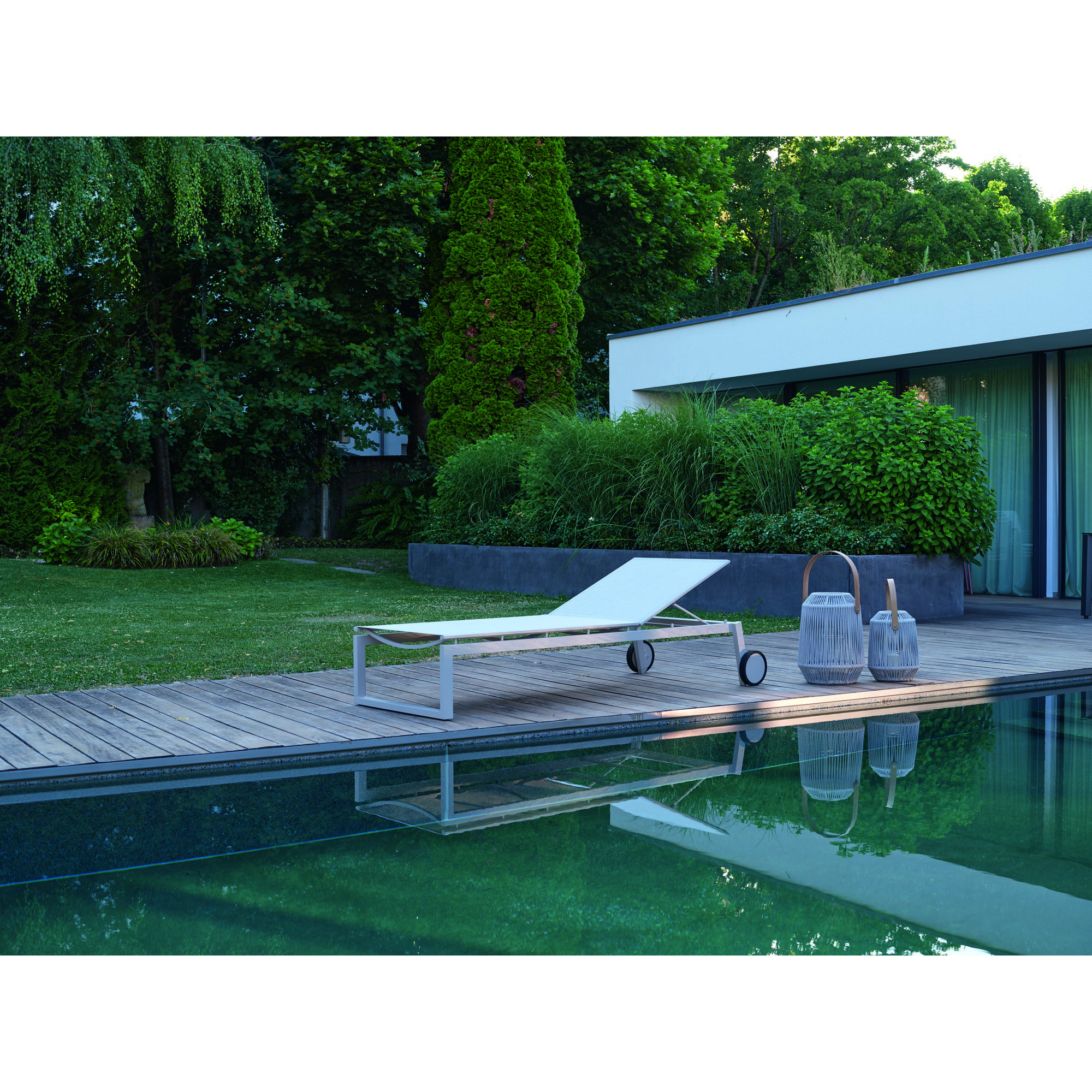 helle Gartenliege auf einer Holzterrasse am Pool mit umliegendem Garten und moderner Hausfassade