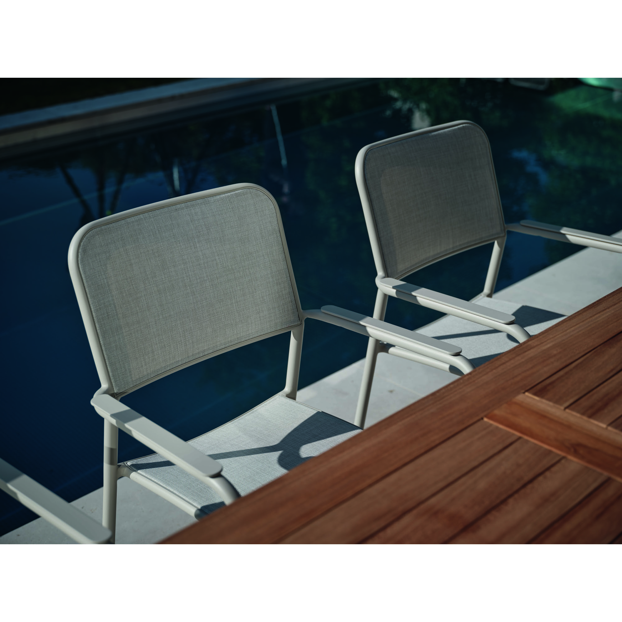 Zwei Gartenstühle mit Armlehnen an Tisch neben Wasserfläche im Außenbereich