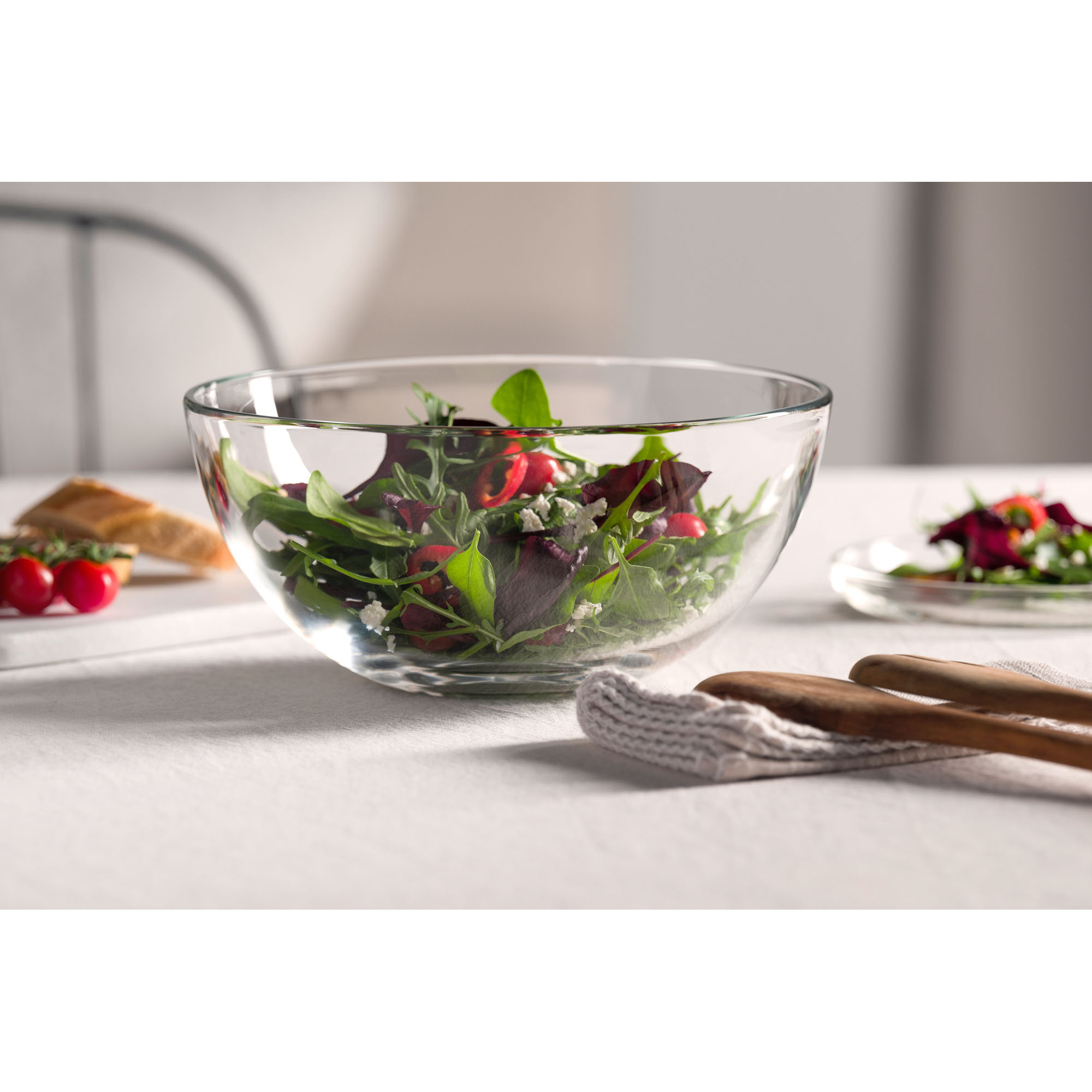 Große Glasschale gefüllt mit gemischtem Salat mit Tomaten und Blättern auf hellem Tisch