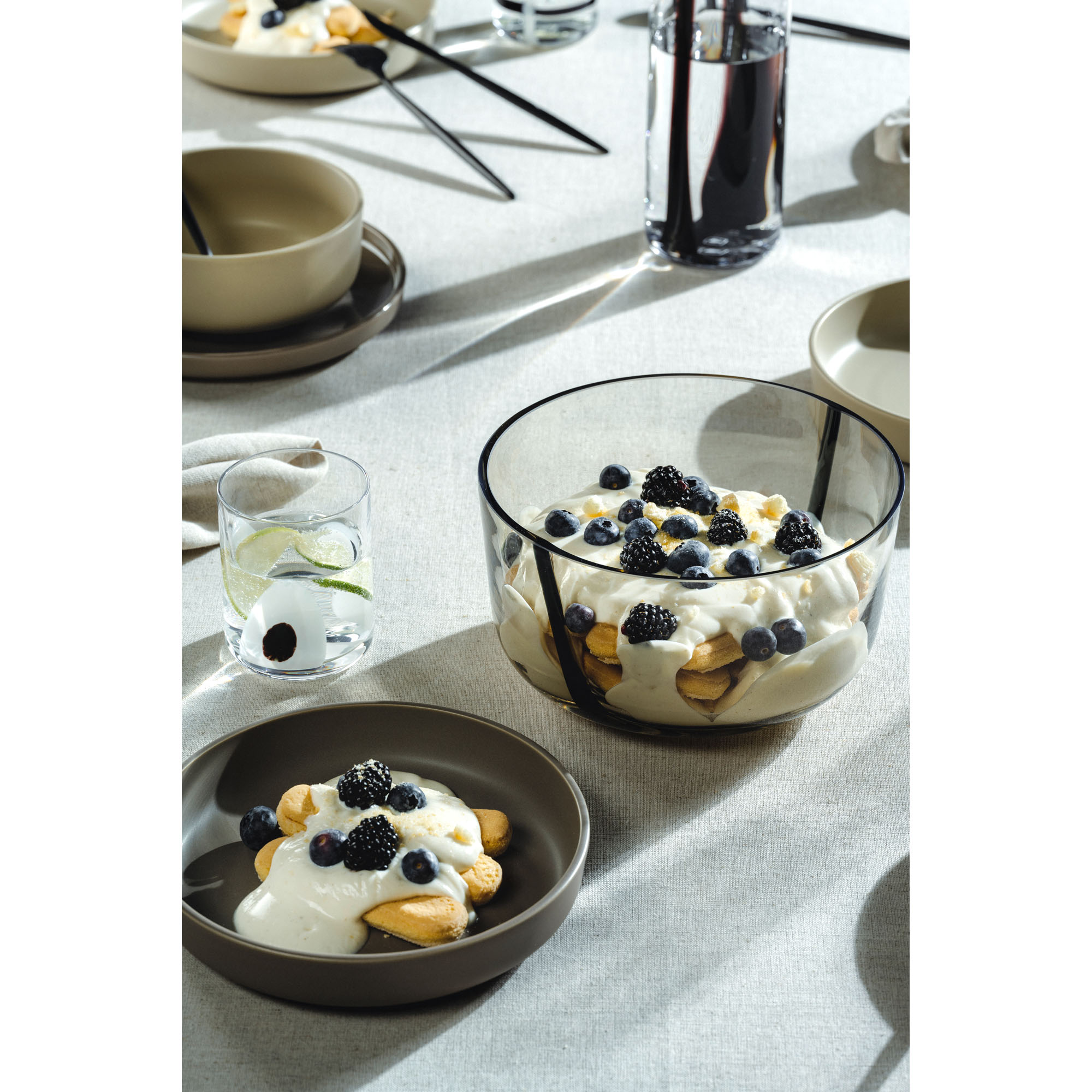Glasschale mit Dessert auf gedecktem Tisch mit Geschirr und Getränken