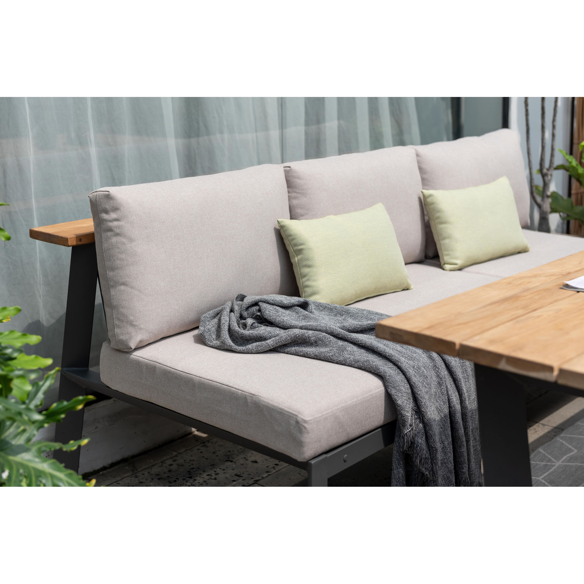 Gartensofa mit hellen Polstern und grünen Kissen, kombiniert mit Holztisch und grauer Decke in stilvoller Outdoor-Umgebung.