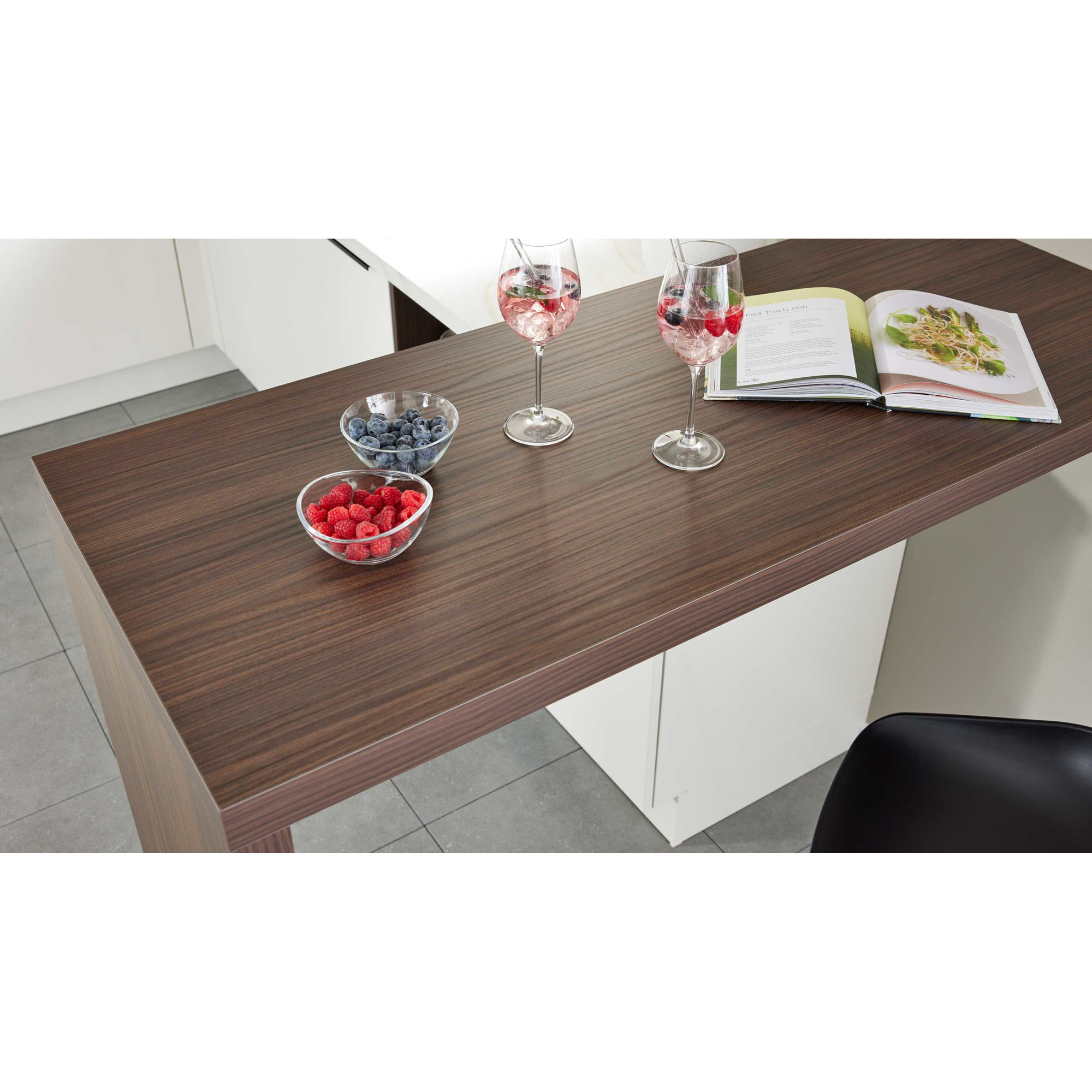 Nahaufnahme einer dunklen Holz-Barplatte mit zwei Weingläsern, Schalen mit Himbeeren und Heidelbeeren sowie einem geöffneten Kochbuch
