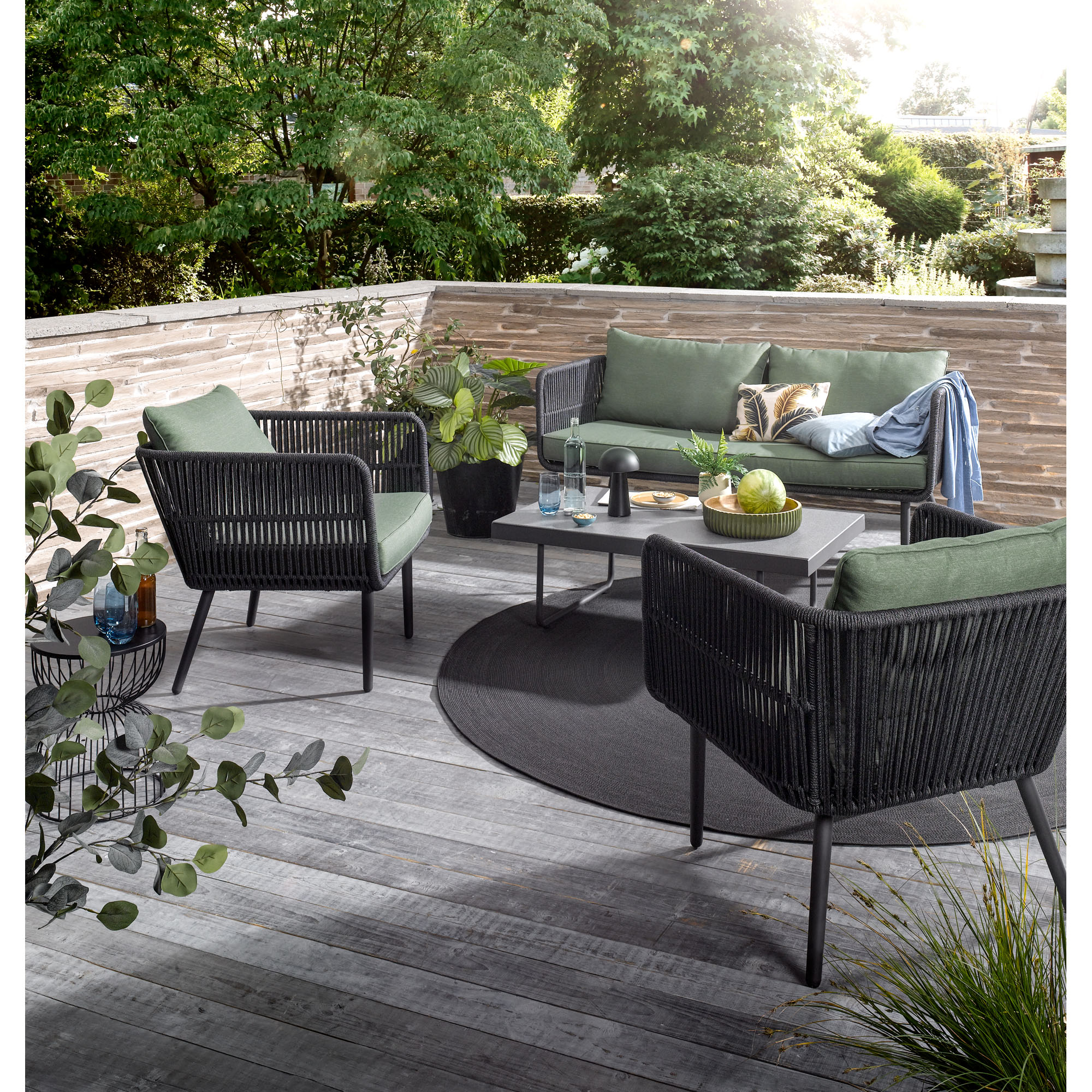 Gartenlounge mit Sofa Sesseln und Tisch auf einer Holzterrasse im Garten