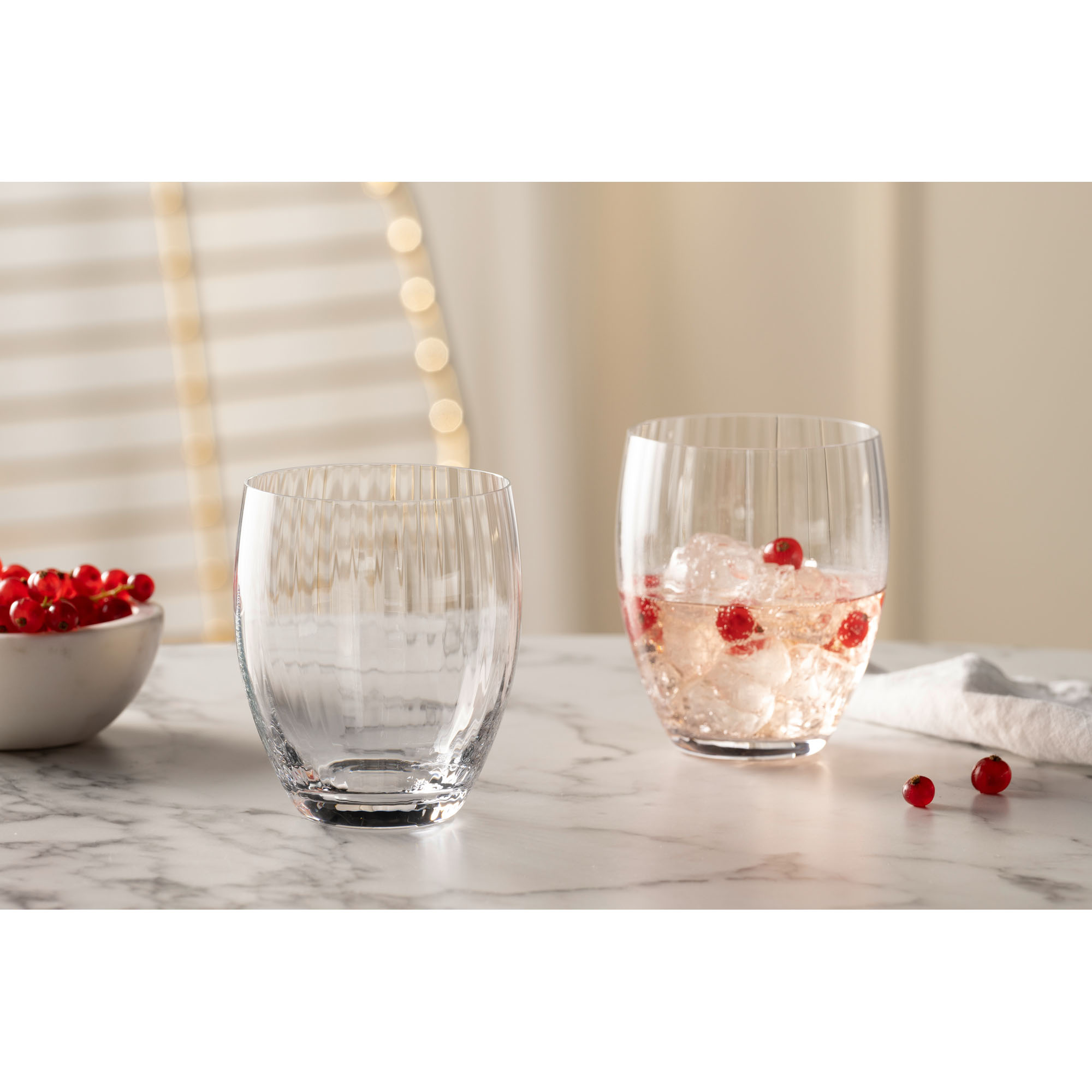 Zwei Trinkgläser eines gefüllt mit Eis und roten Beeren auf hellem Tisch