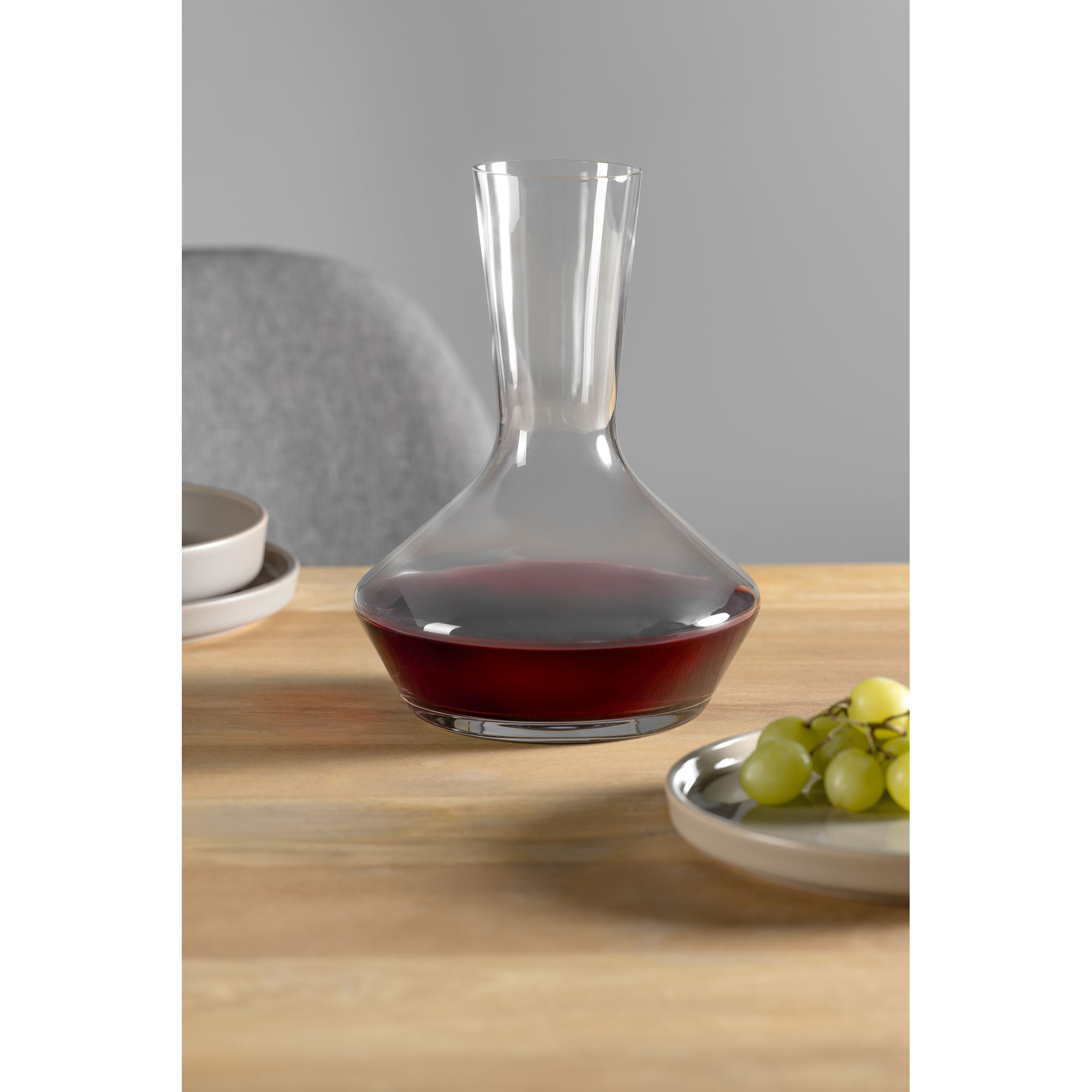 Glaskaraffe gefüllt mit Rotwein auf Tisch neben Trauben und Geschirr