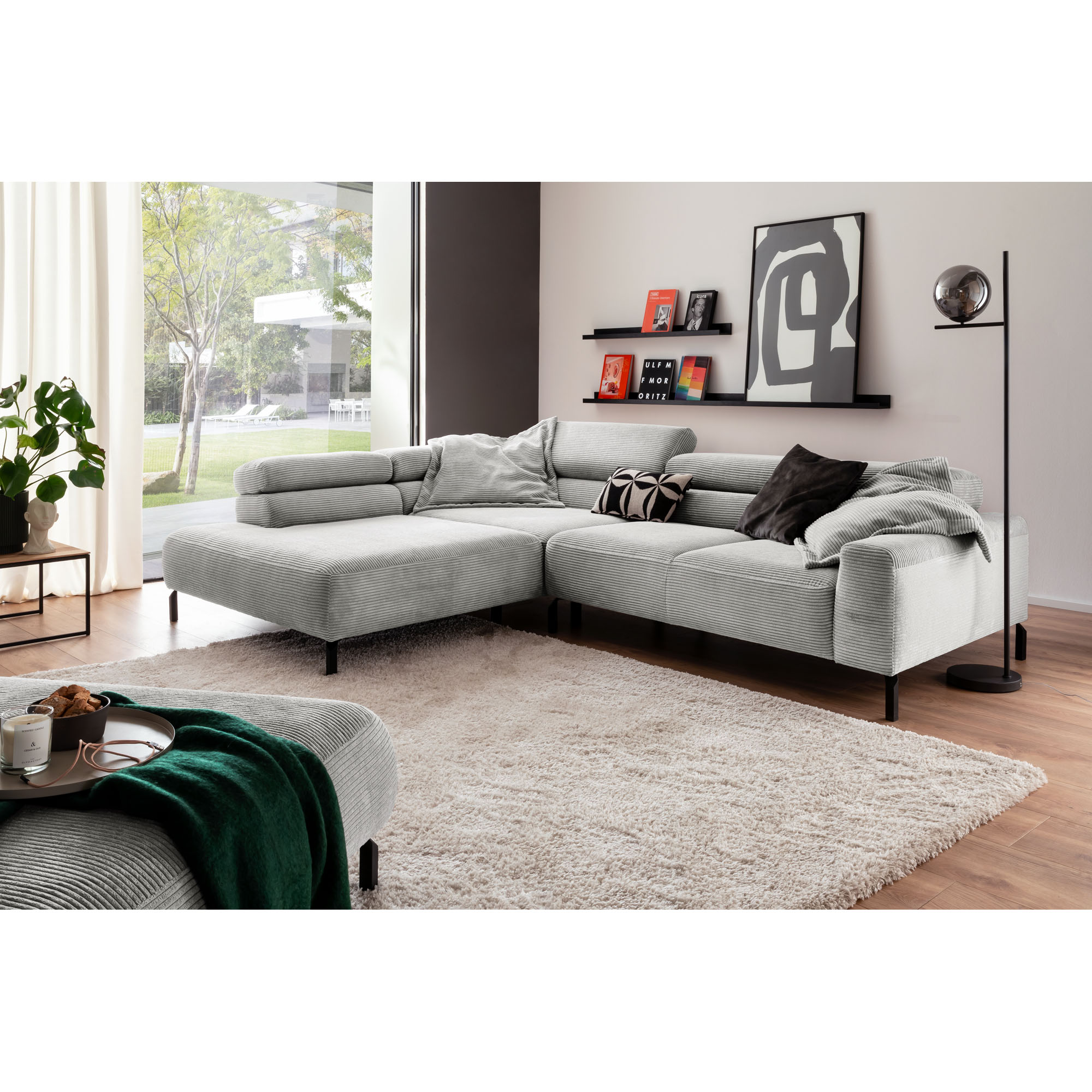 Ecksofa mit Ottomane in Wohnumgebung mit Teppich, Kissen und Wandregalen