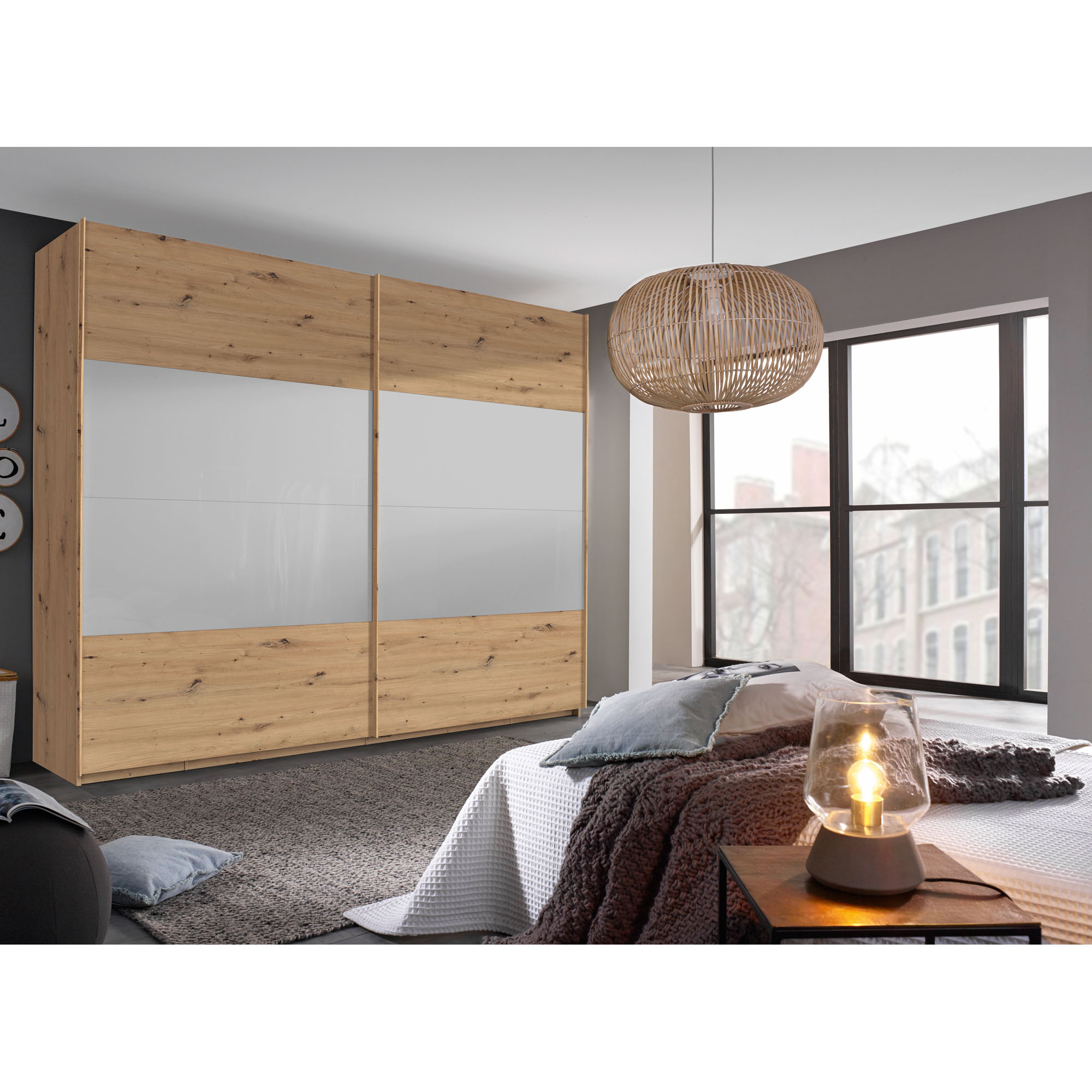 Schwebetürenschrank in Eiche Artisan mit Front in Seidengrau, in Schrägansicht in einem Schlafzimmer-Milieu gezeigt.