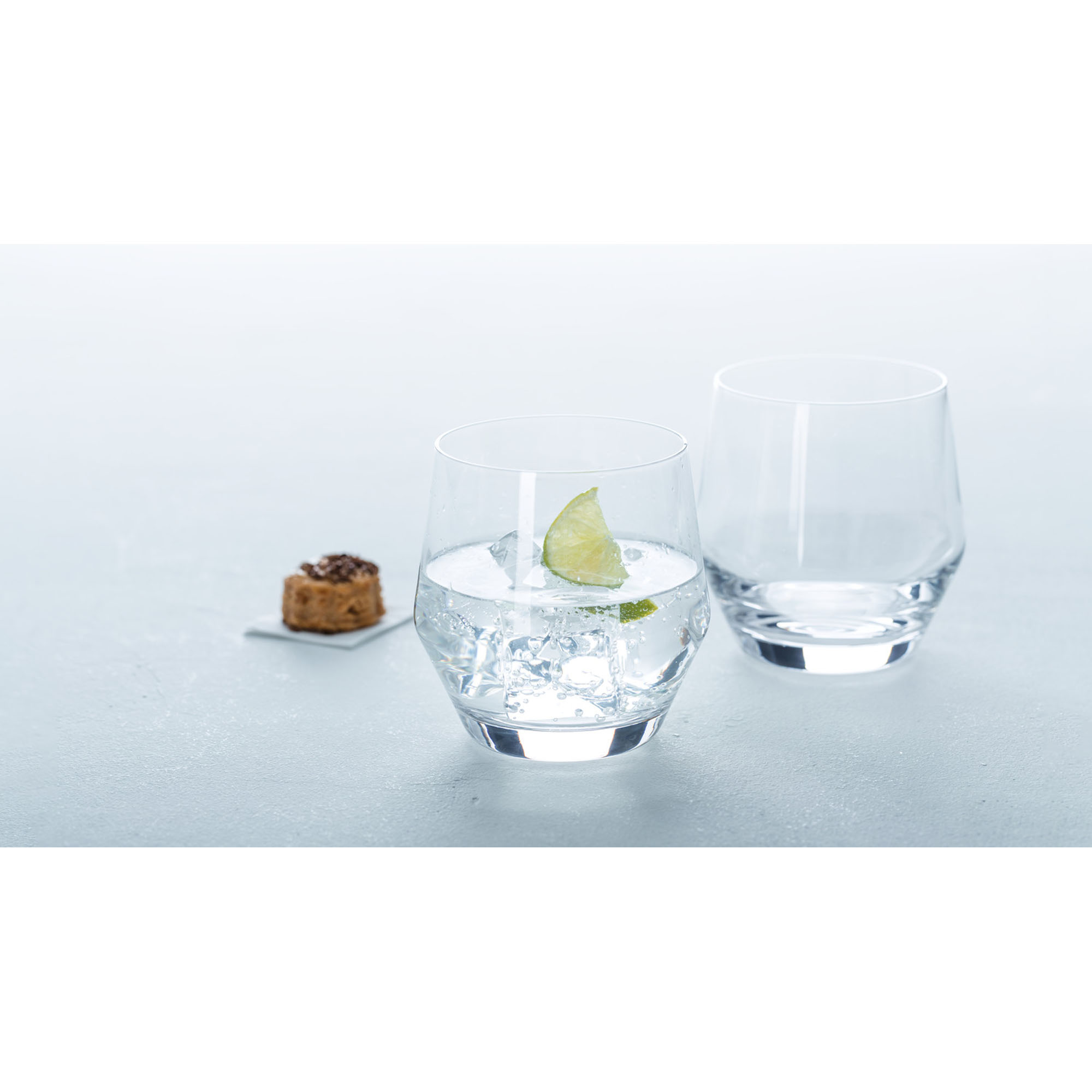 Zwei Trinkgläser mit Wasser Eiswürfeln und Limettenscheibe auf hellem Hintergrund