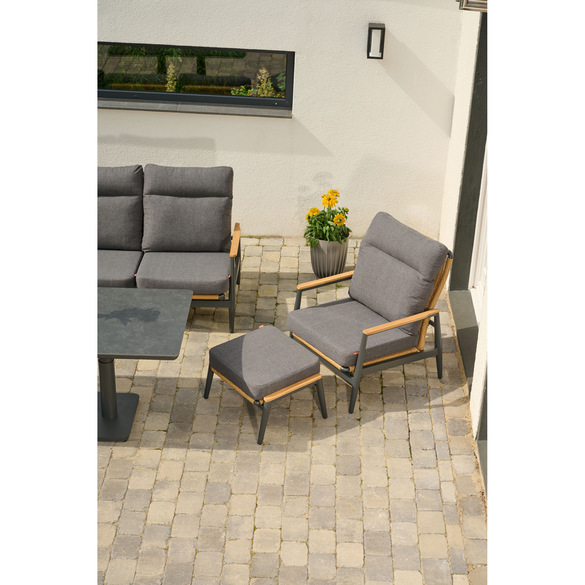 Hocker mit dunkelgrauem Polster, kombiniert mit passendem Sessel und Gartenset auf einer Terrasse