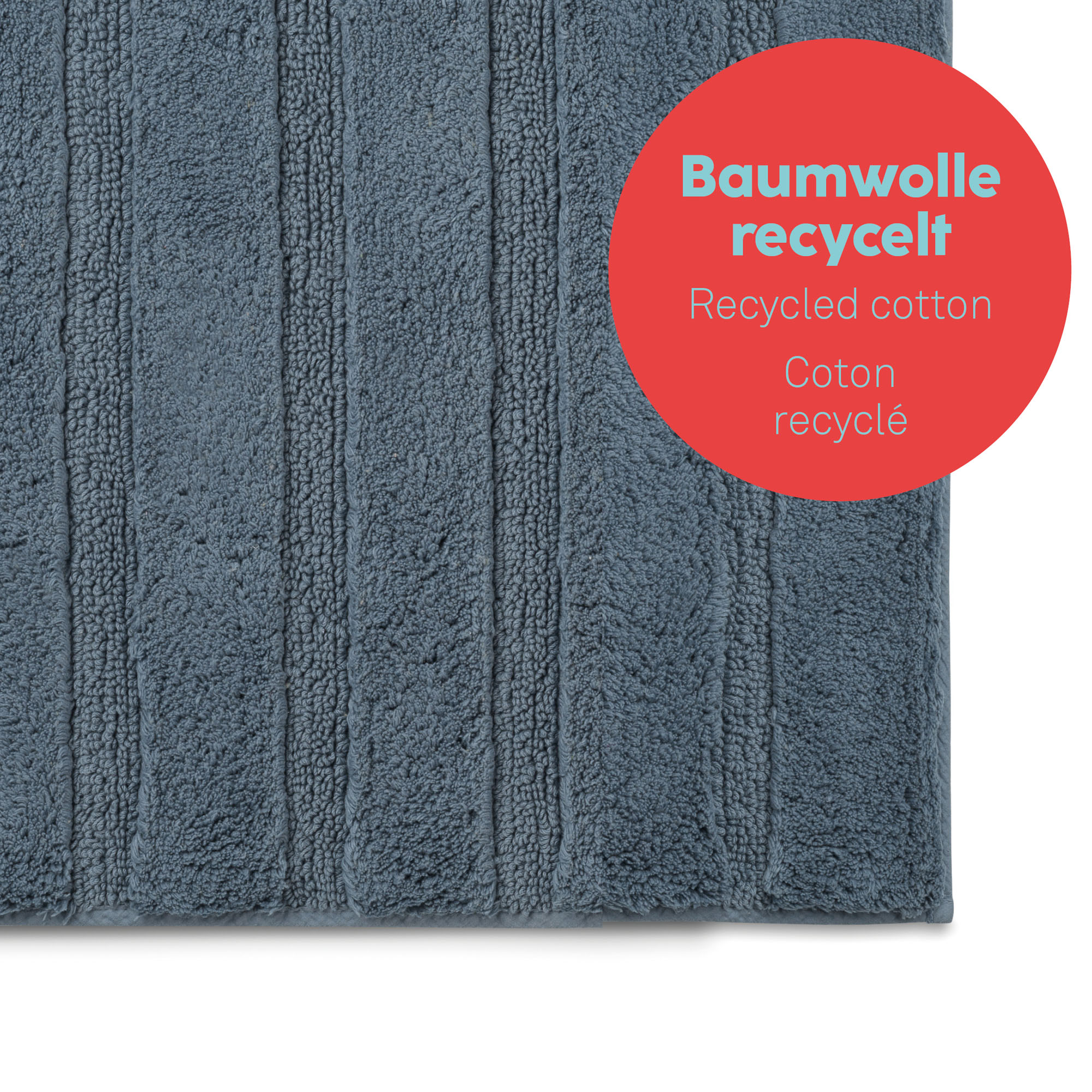 Vergrößerte Ansicht der rauchblauen Bademattenoberfläche mit länglichen Rippen und rotem Hinweisfeld zum Baumwollmaterial