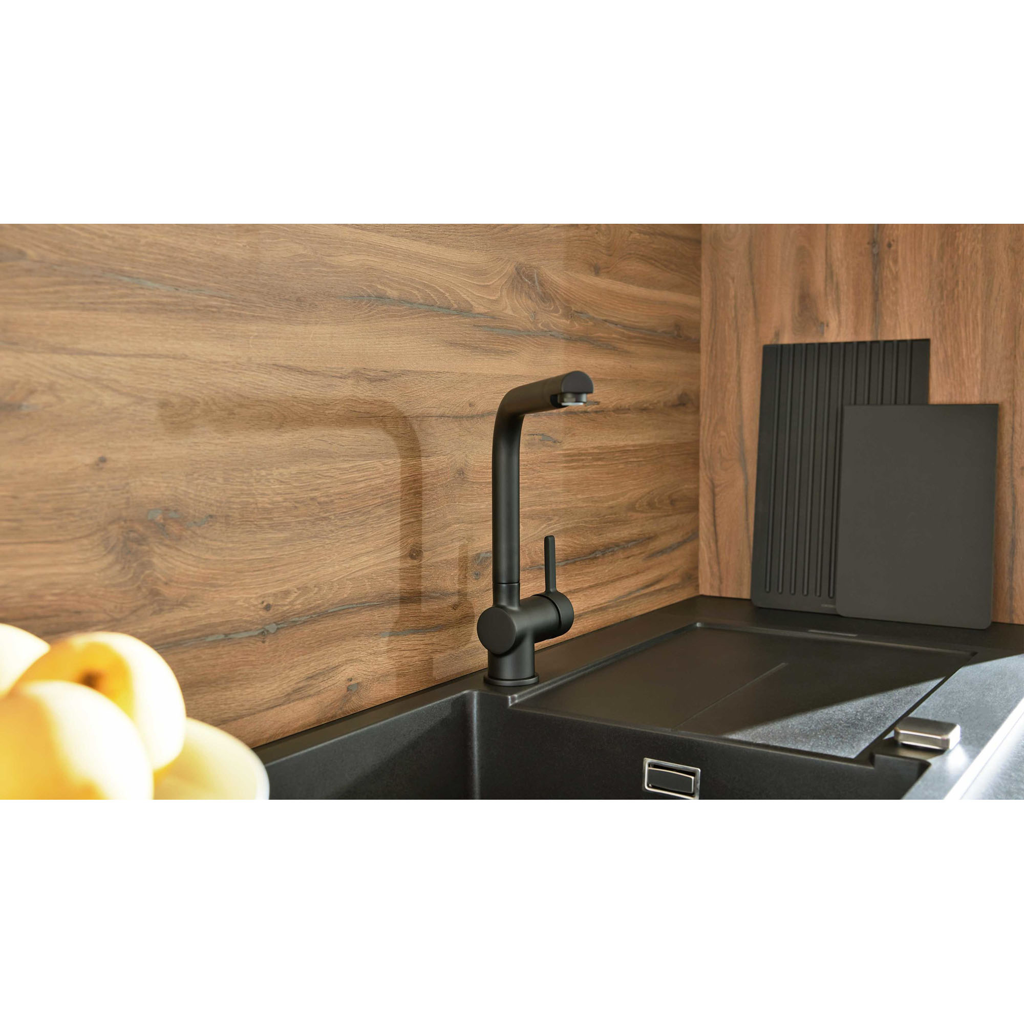 Nahaufnahme einer dunklen Küchenarmatur vor einer warmen Holzrückwand mit Abdeckplatte und Küchenzubehör