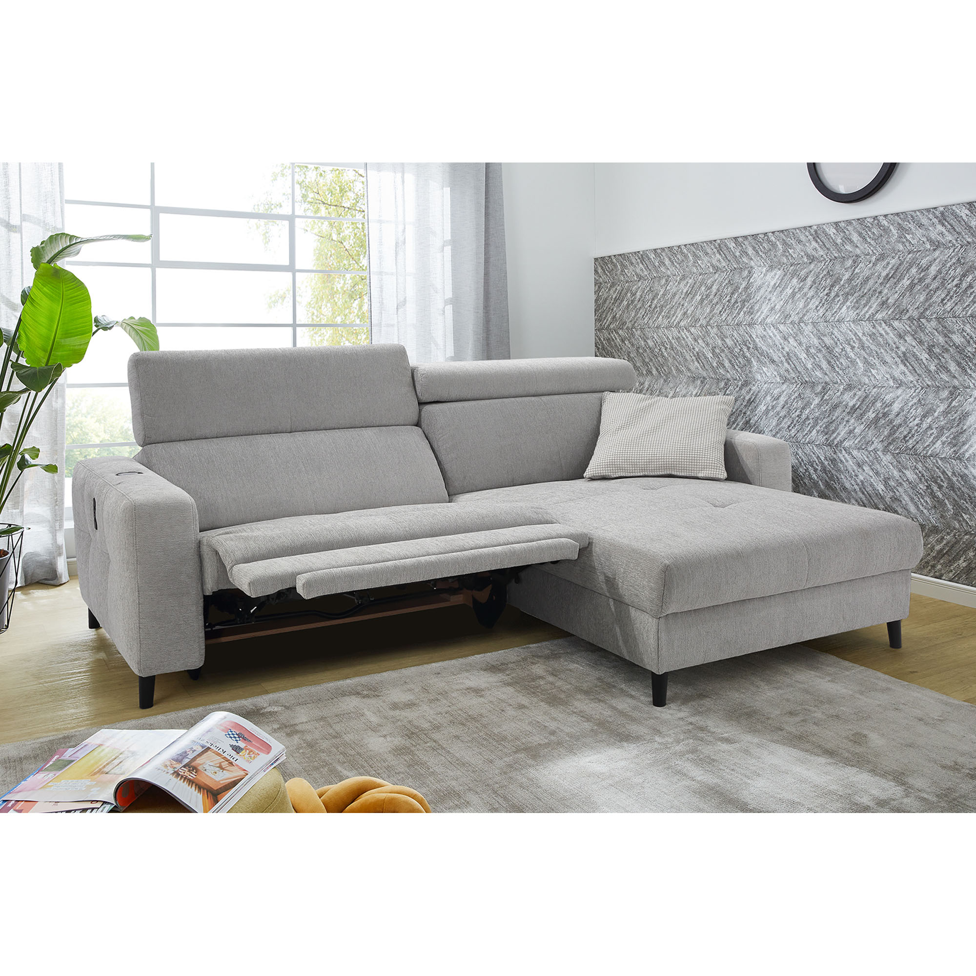 Modernes Ecksofa mit ausgefahrener Relaxfunktion und Ottomane in heller Wohnzimmereinrichtung