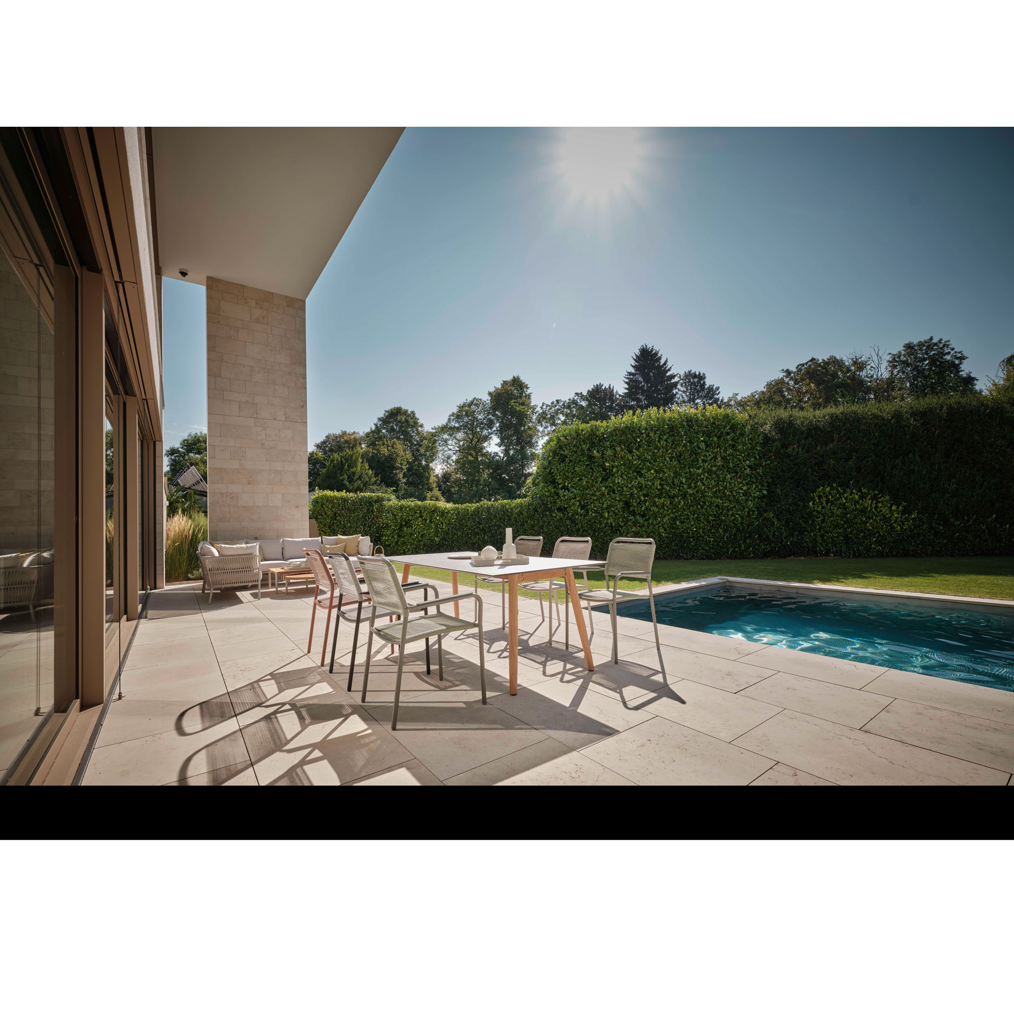 Mehrere Gartenstühle an Tisch auf Terrasse neben Pool und Grünfläche