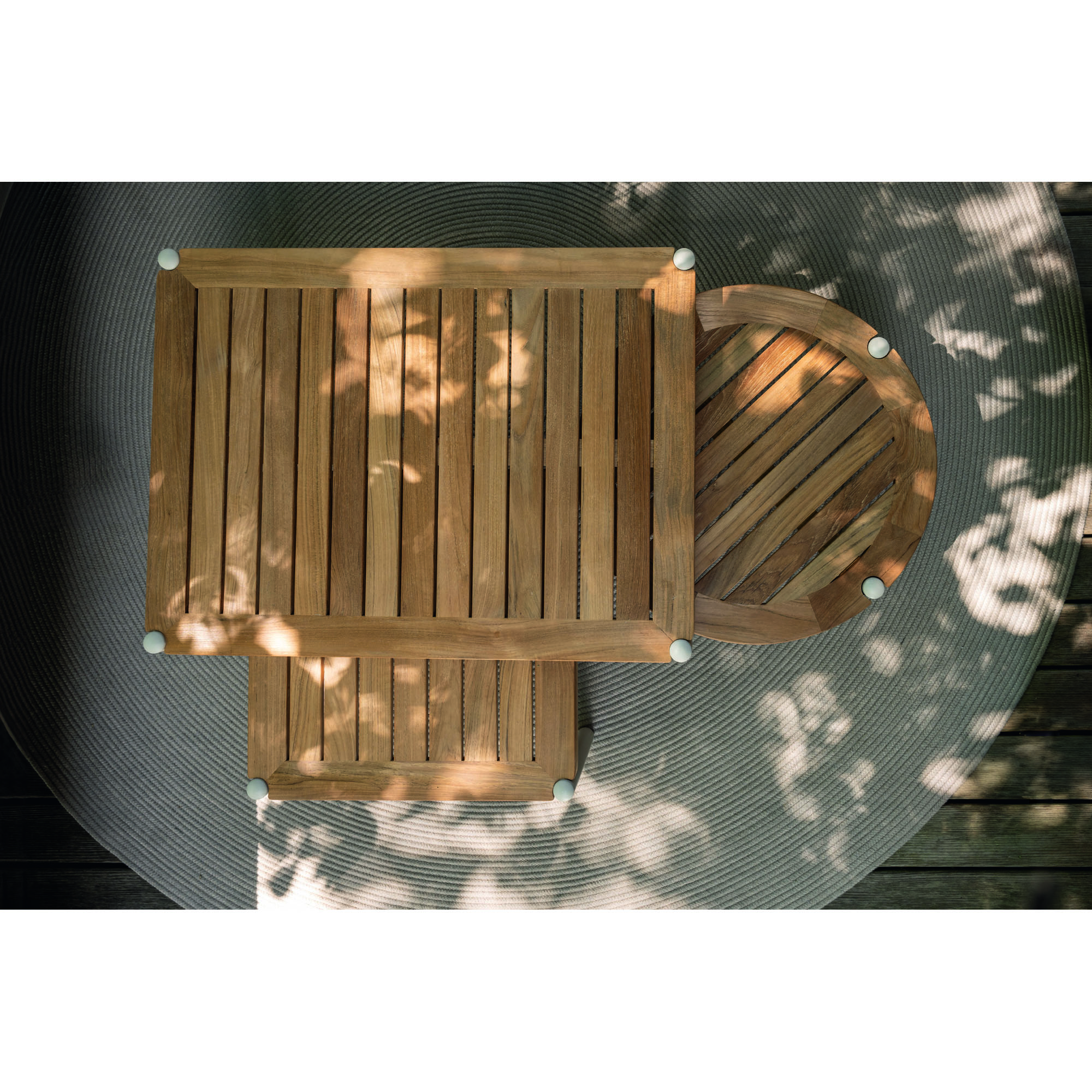 Draufsicht auf zwei quadratische und einen runden Beistelltisch aus Holz auf einem runden Outdoor-Teppich