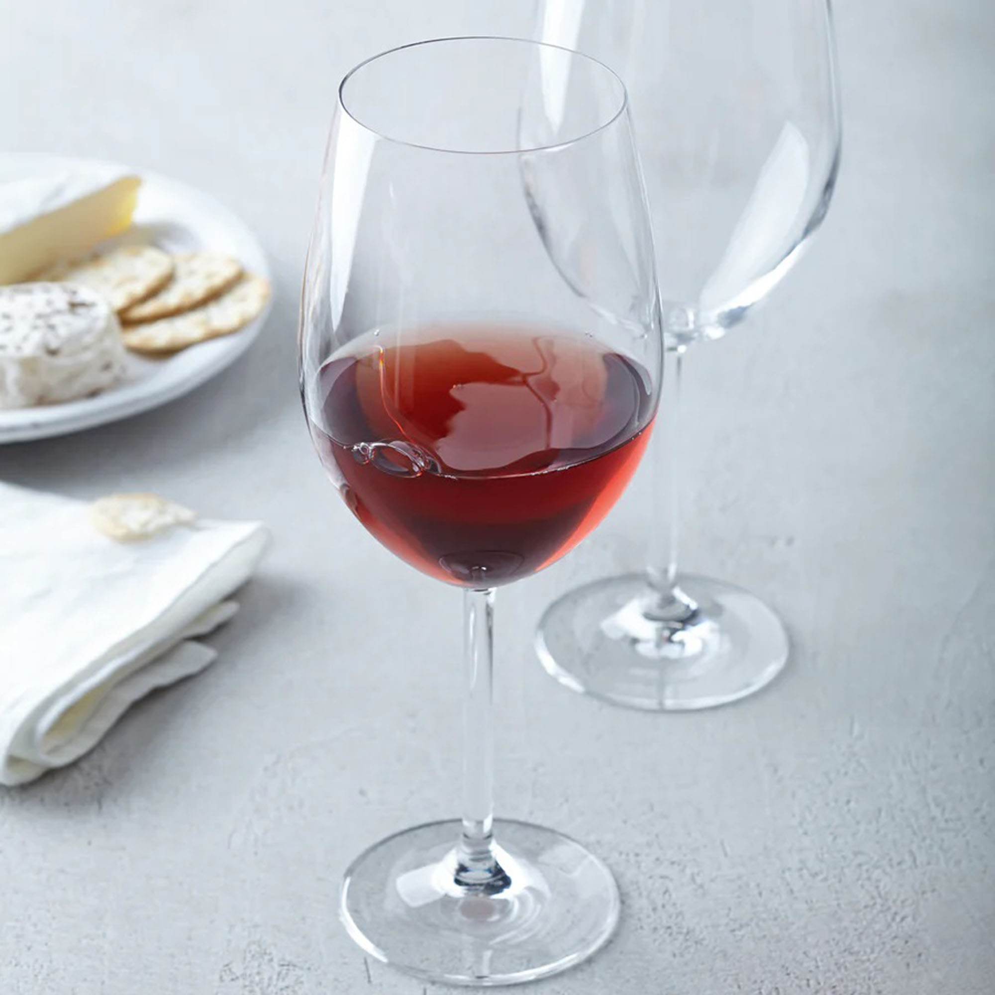 Weißweinglas mit roséfarbenem Wein auf Tisch daneben Käse und Gebäck im Hintergrund