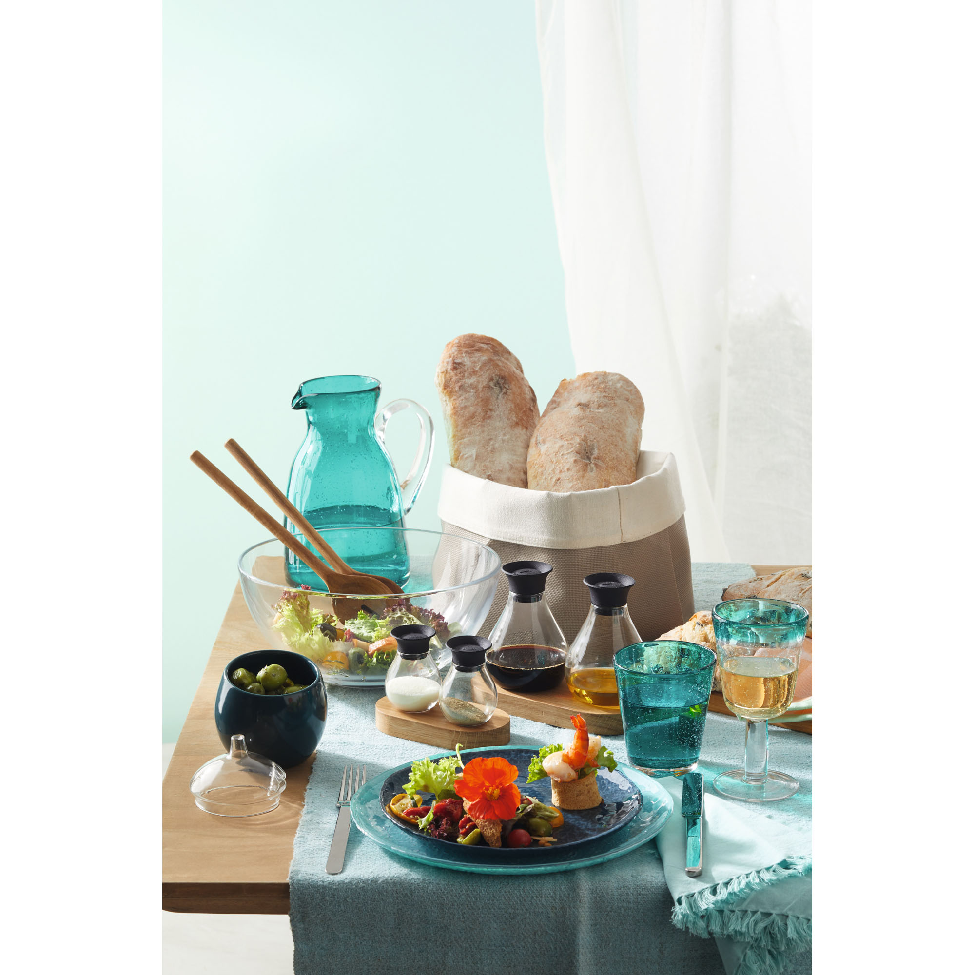 Gedeckter Tisch mit Glasschalen Tellern und Gläsern sowie Brot und Speisen in stilvollem Arrangement