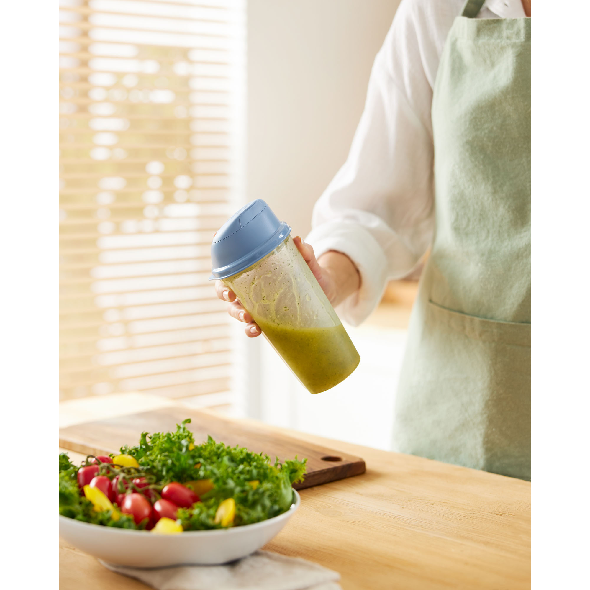 Transparenter Shaker mit blauem Deckel wird über einer Salatschüssel gehalten