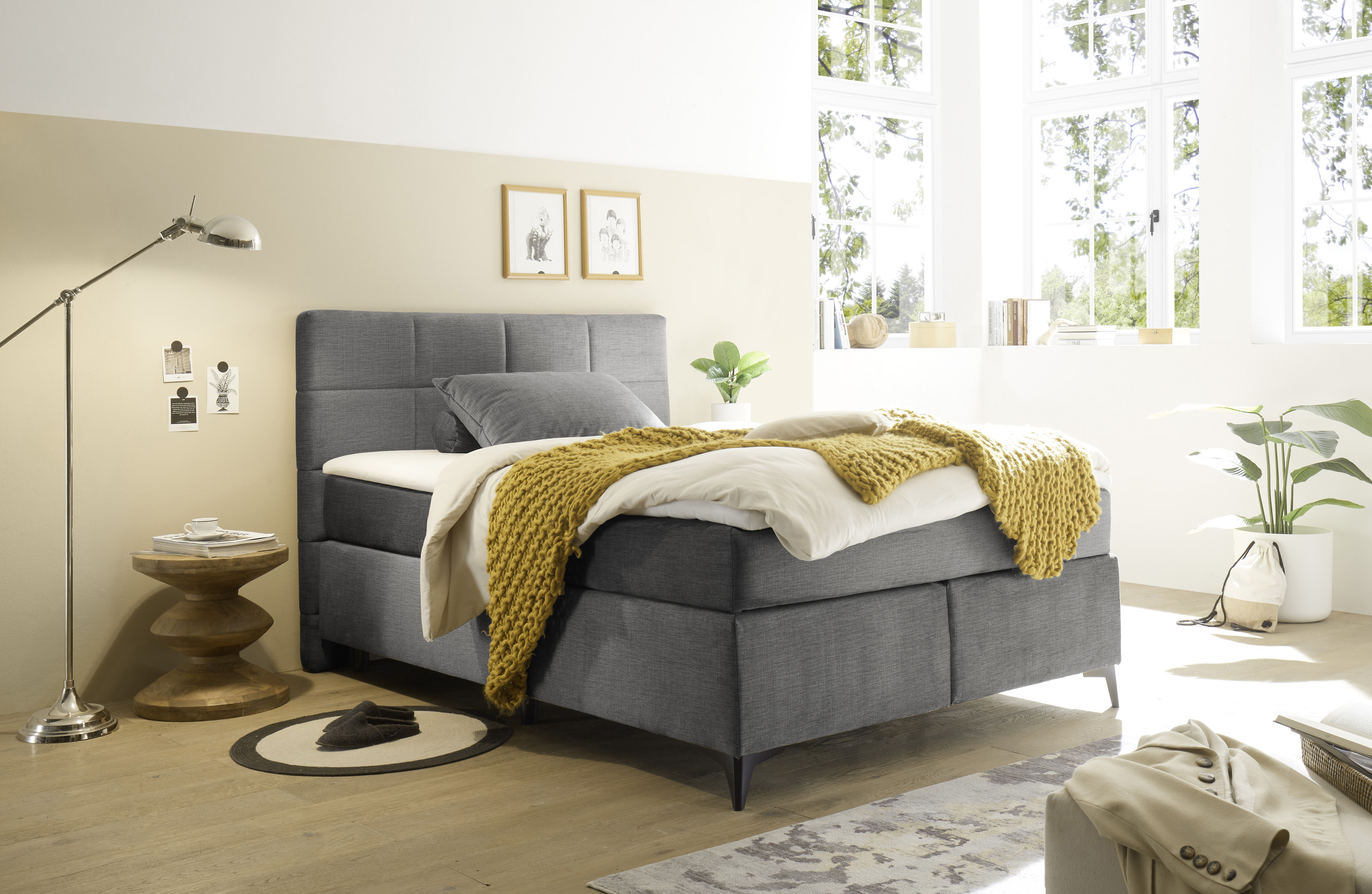Boxspringbett „Voss 15 grey“ in einem eingerichteten Schlafzimmer, mit Kissen und Bettdecke ausgestattet, in wohnlichem Ambiente präsentiert