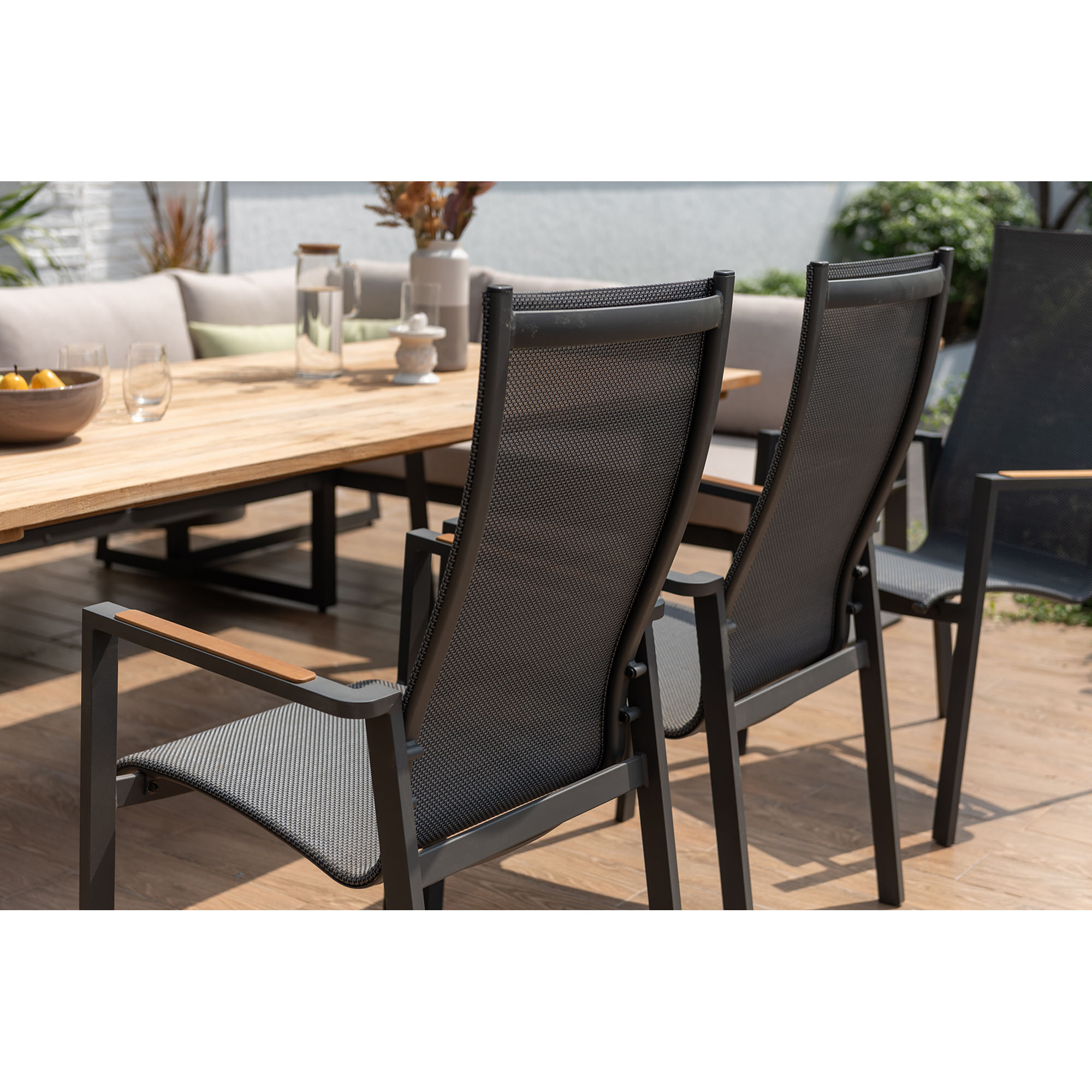 Mehrere Gartenstühle mit hoher Rückenlehne und Textilbespannung an einem Holztisch auf einer Terrasse