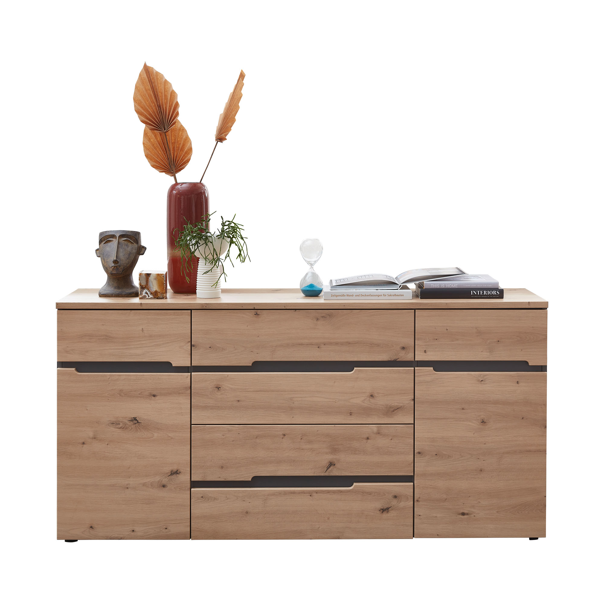 Holzsideboard mit mehreren Schubladen und Türen; darauf stehen Vasen, ein Kopfobjekt, eine Pflanze, eine Sanduhr und ein geöffnetes Buch.