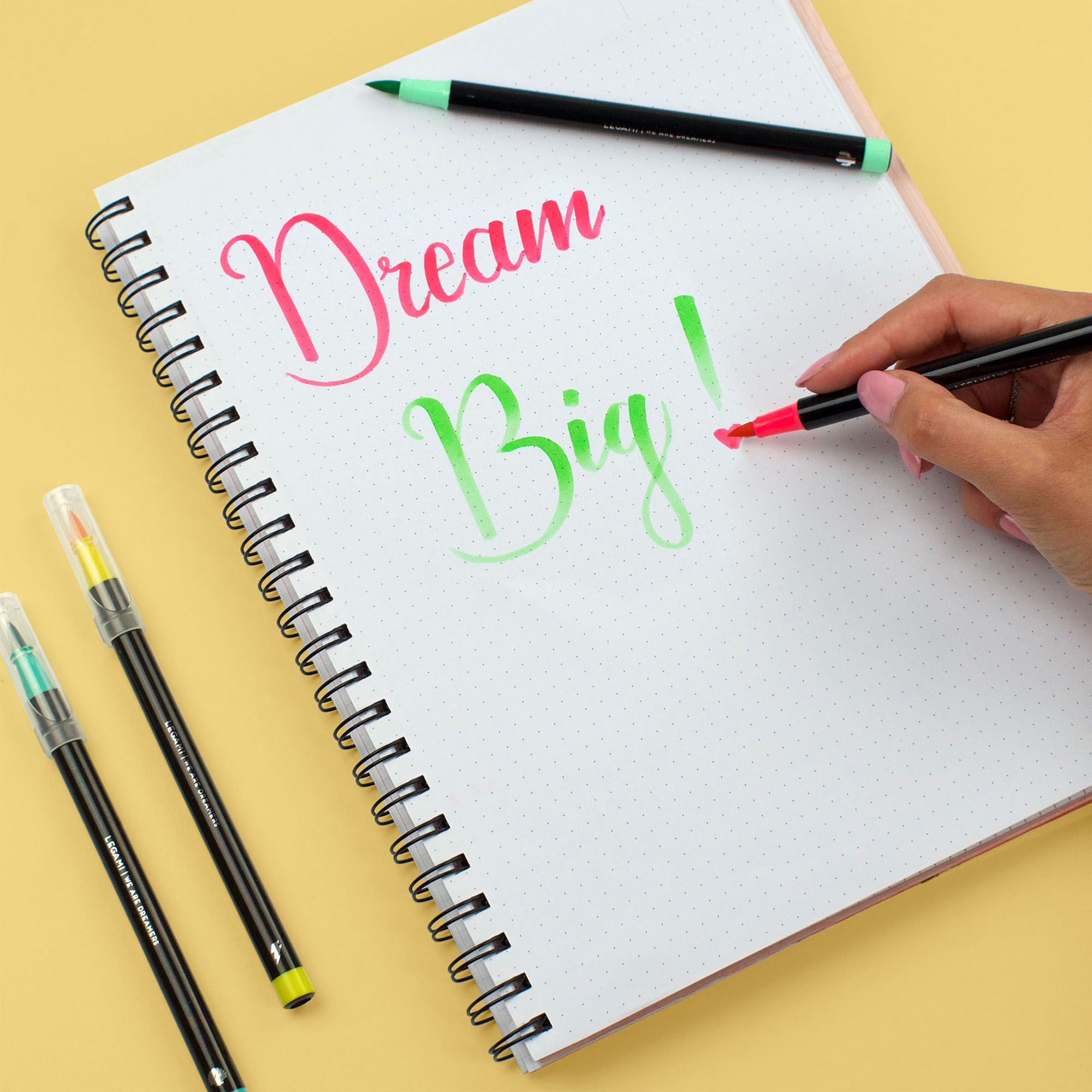 Zwölf Brushpens in kräftigen Farben, bei einer Handlettering-Anwendung auf einem Notizblock gezeigt.