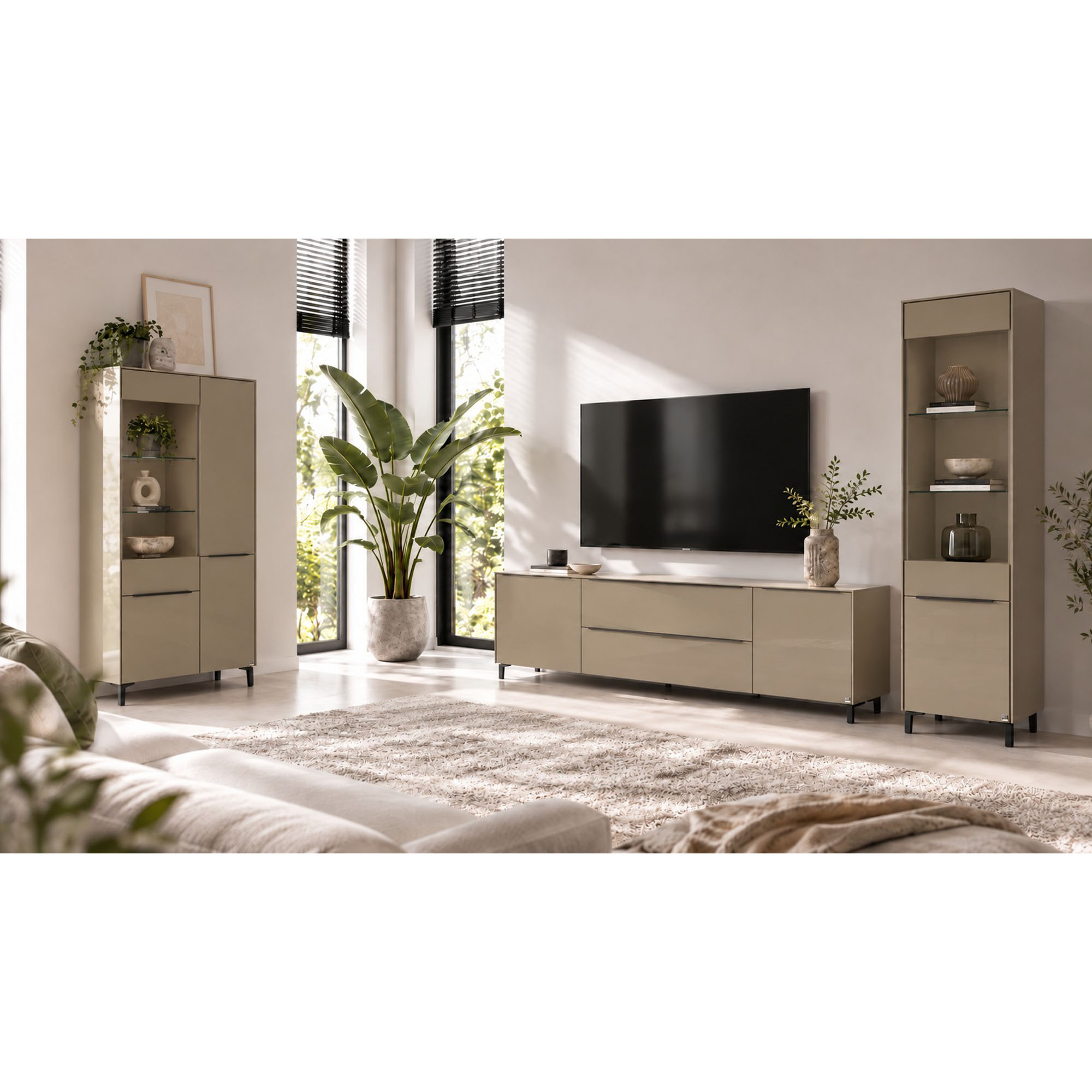 Helles Wohnzimmer mit einer schmalen taupefarbenen Vitrine rechts neben einem Lowboard mit Fernseher. Die Vitrine besitzt offene Glasablagen mit dekorativen Vasen und Schalen sowie ein geschlossenes Fach im unteren Bereich. Links im Raum steht eine breite