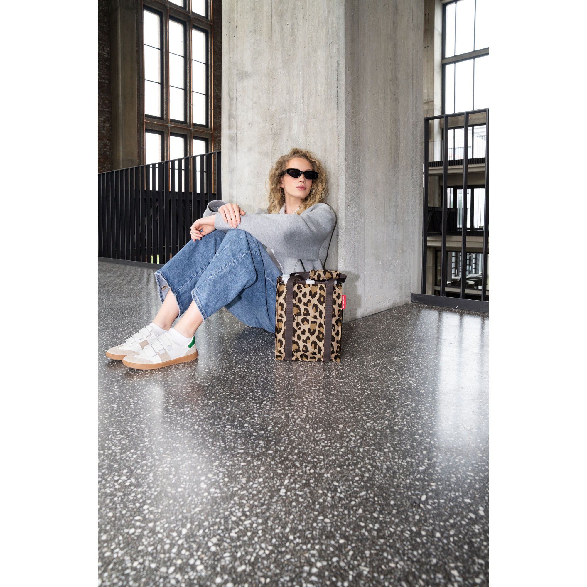 Flaschentasche von Reisenthel, Modell Bottlebag, in Beige und Braun mit Leopardenmuster, neben einer sitzenden Person mit eingesetzten Flaschen.
