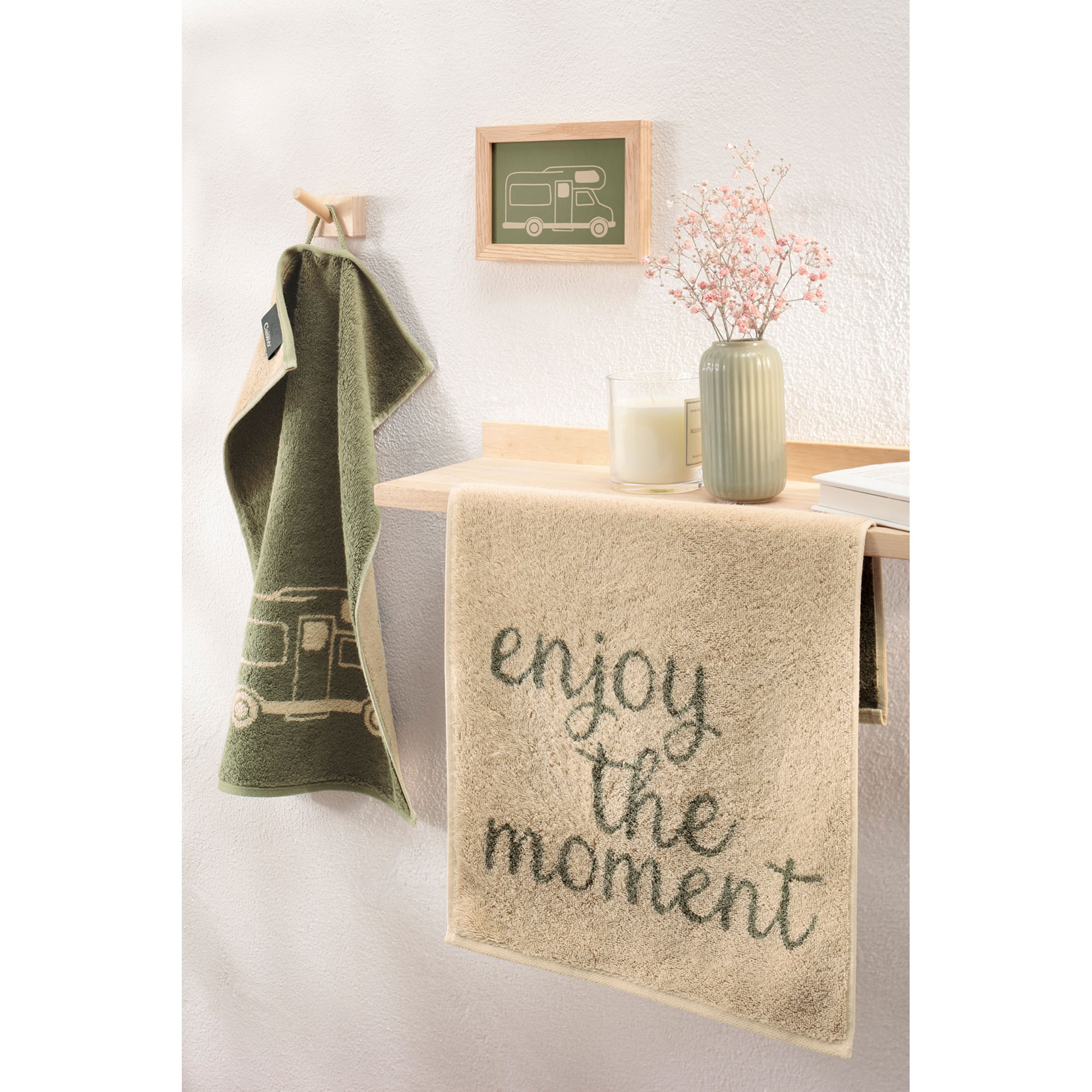 Beiges Gästetuch mit dem Schriftzug „enjoy the moment“ hängt an einem Waschplatz, daneben ein olivfarbenes Motivtuch.