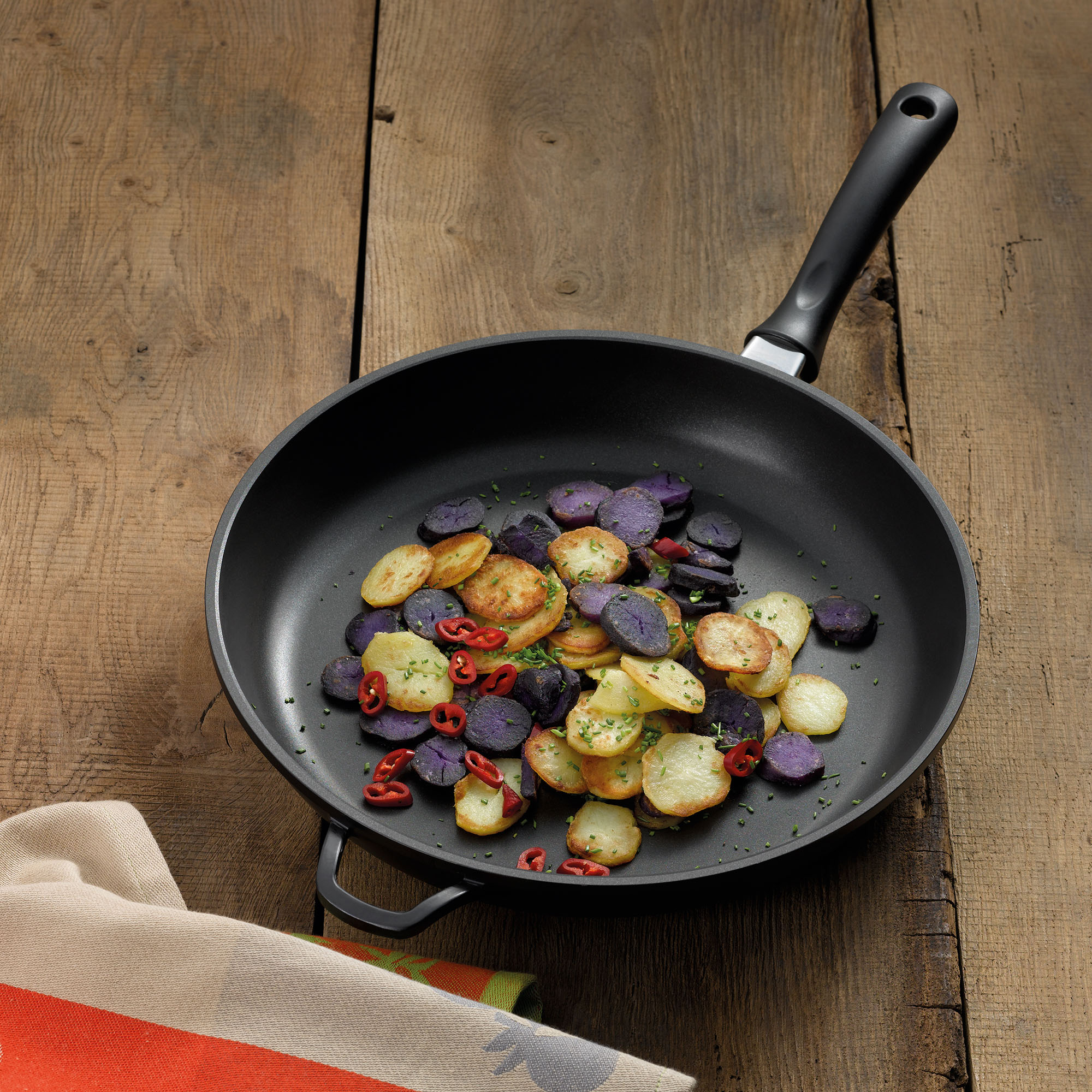 Bratpfanne mit gebratenen Kartoffeln und Gemüse auf einer rustikalen Holzfläche