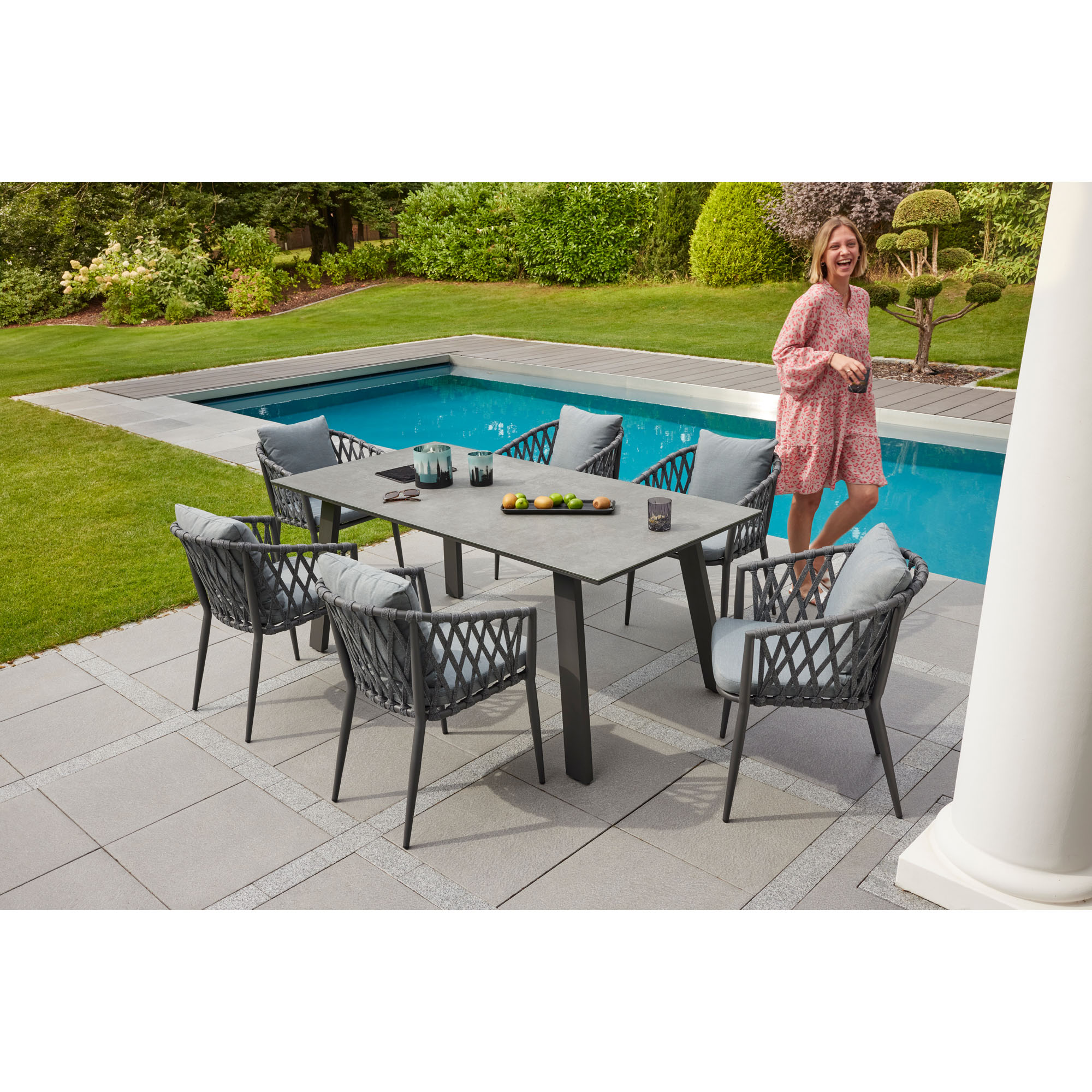 Rechteckiger Gartentisch mit mehreren Gartenstühlen auf einer Terrasse neben einem Pool