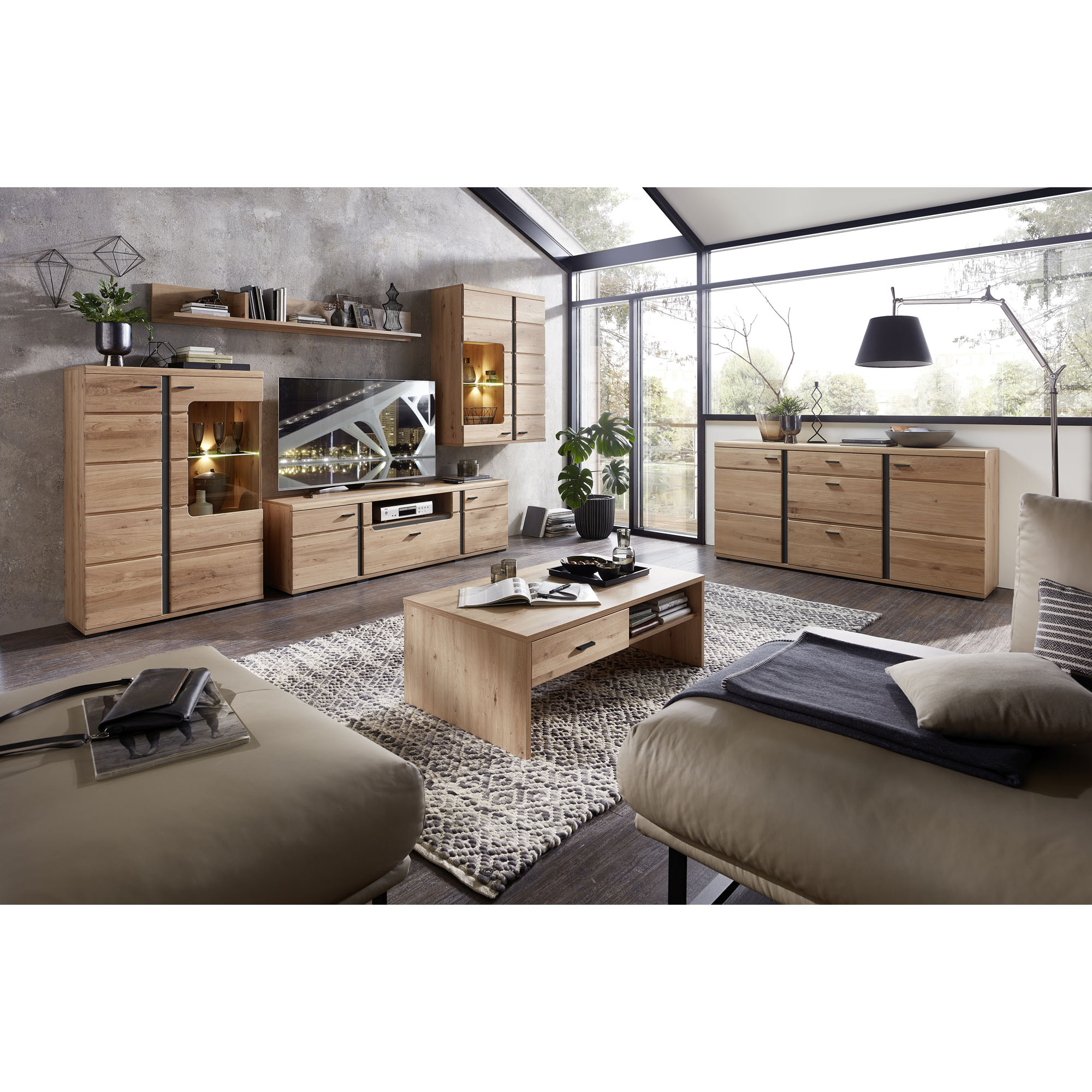 Moderner Wohnraum mit Couchtisch aus hellem Holz, Sofas und einer beleuchteten Wohnwand; große Fenster geben den Blick auf Außenbereich und Natur frei.