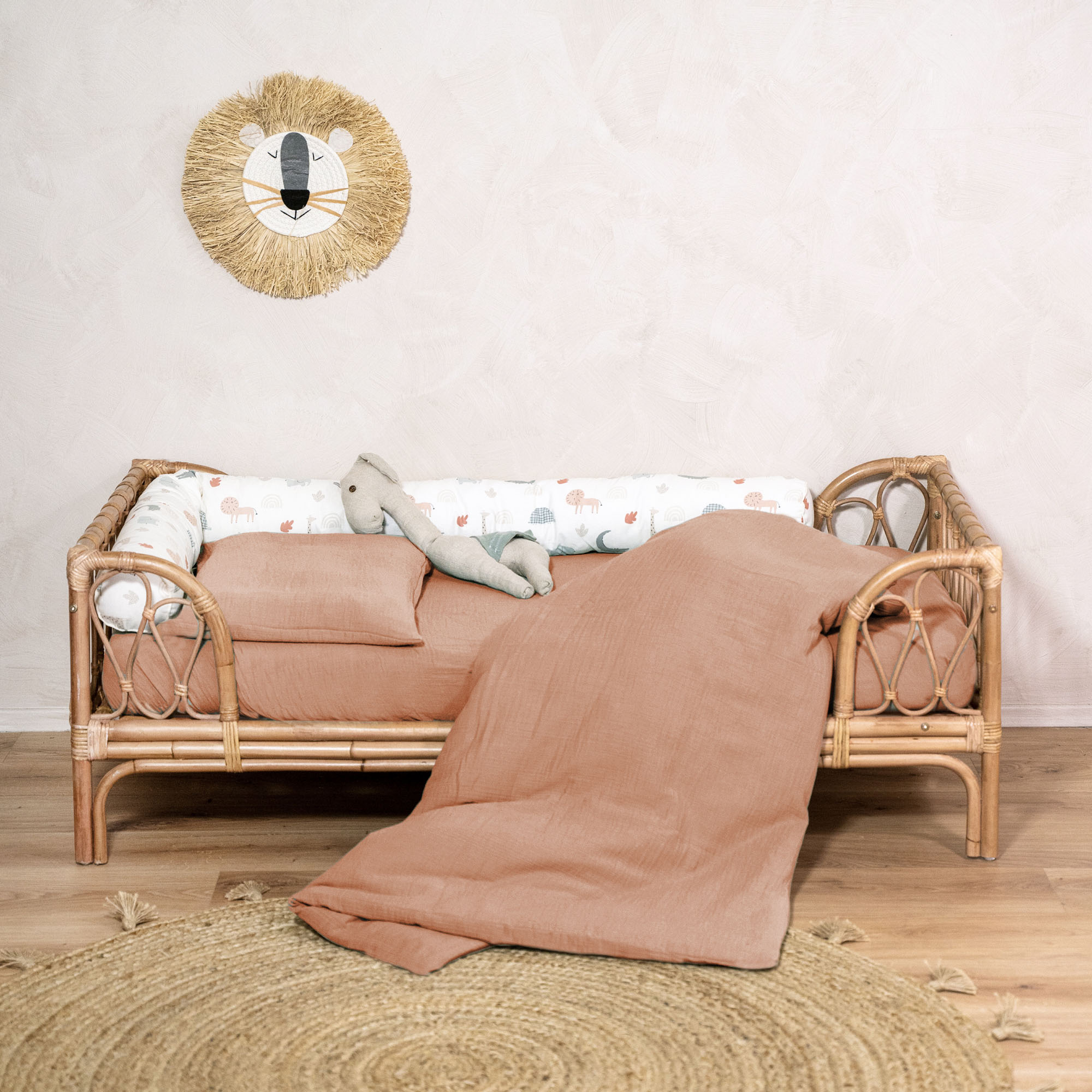 Kinderbett aus Rattan mit Bettwäsche in Terrakotta, Stofftier und Rundteppich aus Jute in einem liebevoll eingerichteten Kinderzimmer