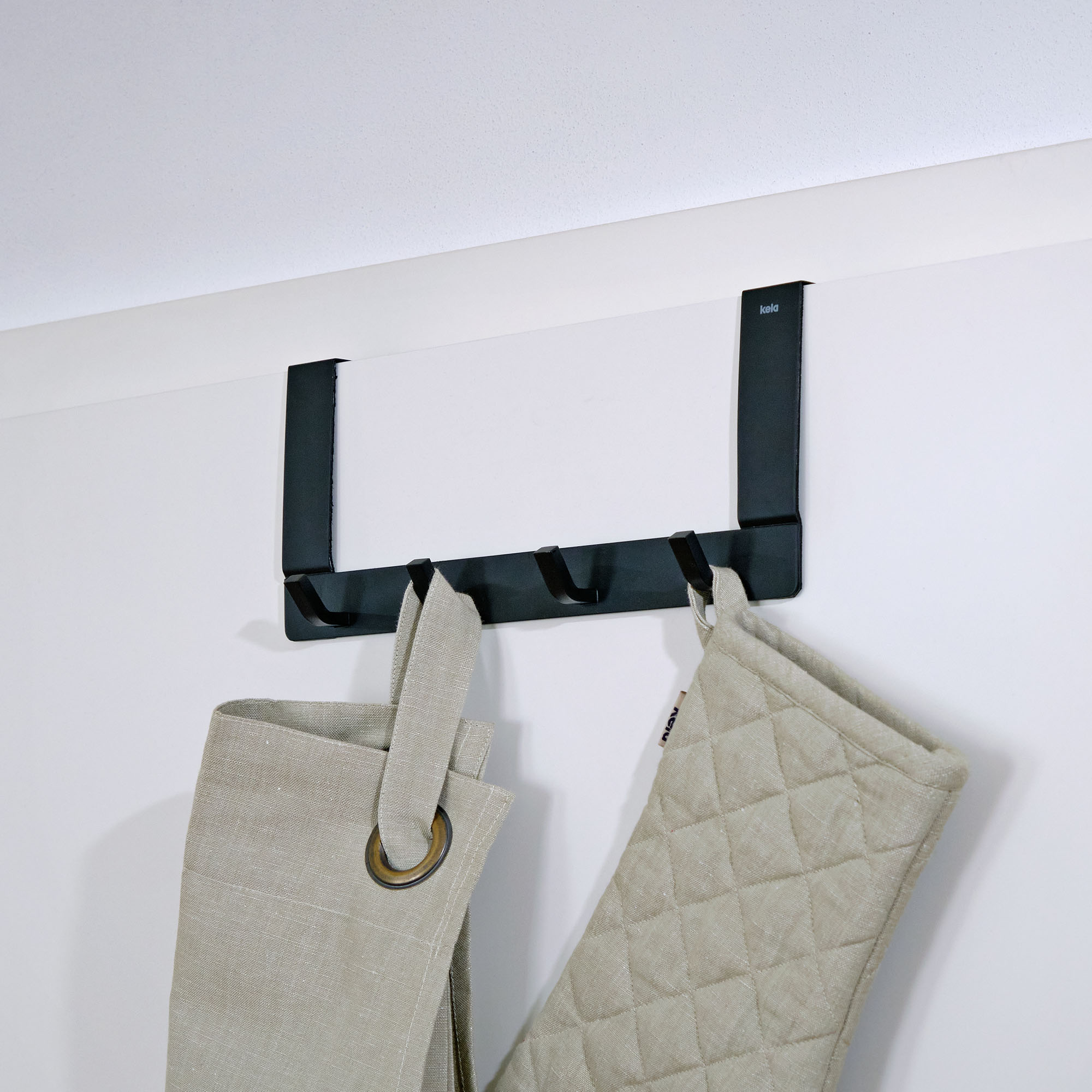 Schwarze Türgarderobe an einer weißen Tür mit zwei aufgehängten hellen Textilien
