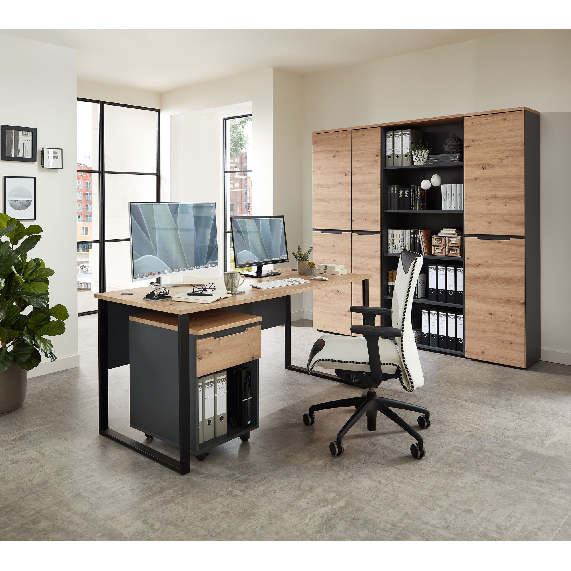 Büroraumszene mit Schreibtisch, zwei Monitoren und einem großen Schrank in Holzoptik im Hintergrund