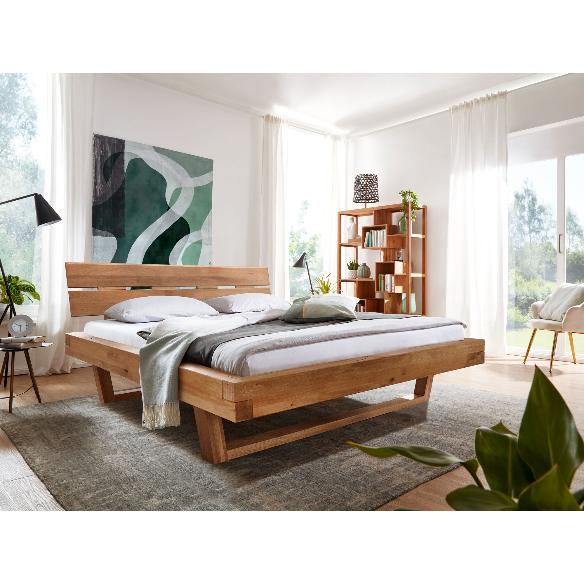 Doppelbett aus massivem Holz mit geneigtem Kopfteil in einem hellen Schlafzimmer mit Regal und großen Fenstern
