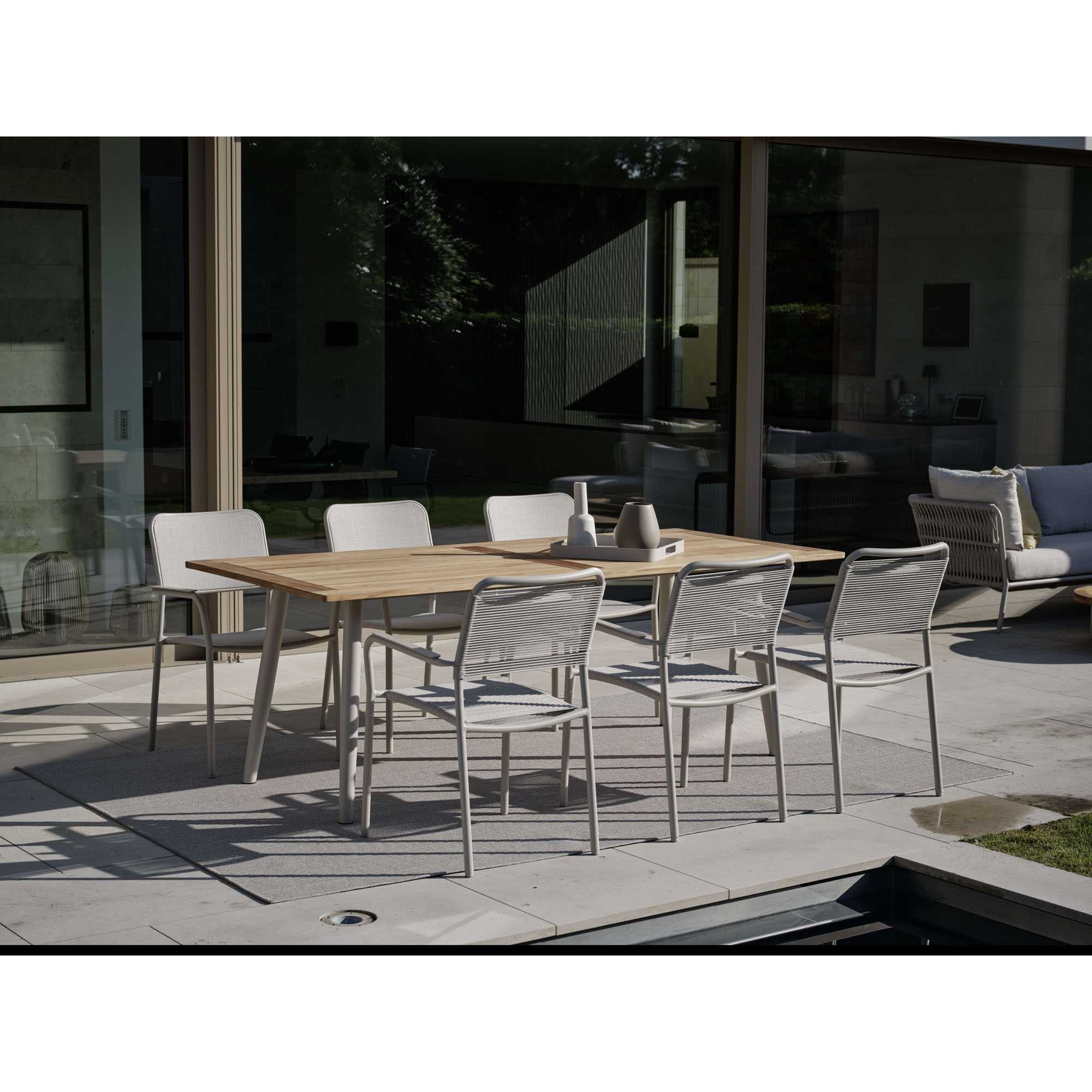 Mehrere Gartenstühle an rechteckigem Tisch auf Terrasse vor Glasfassade