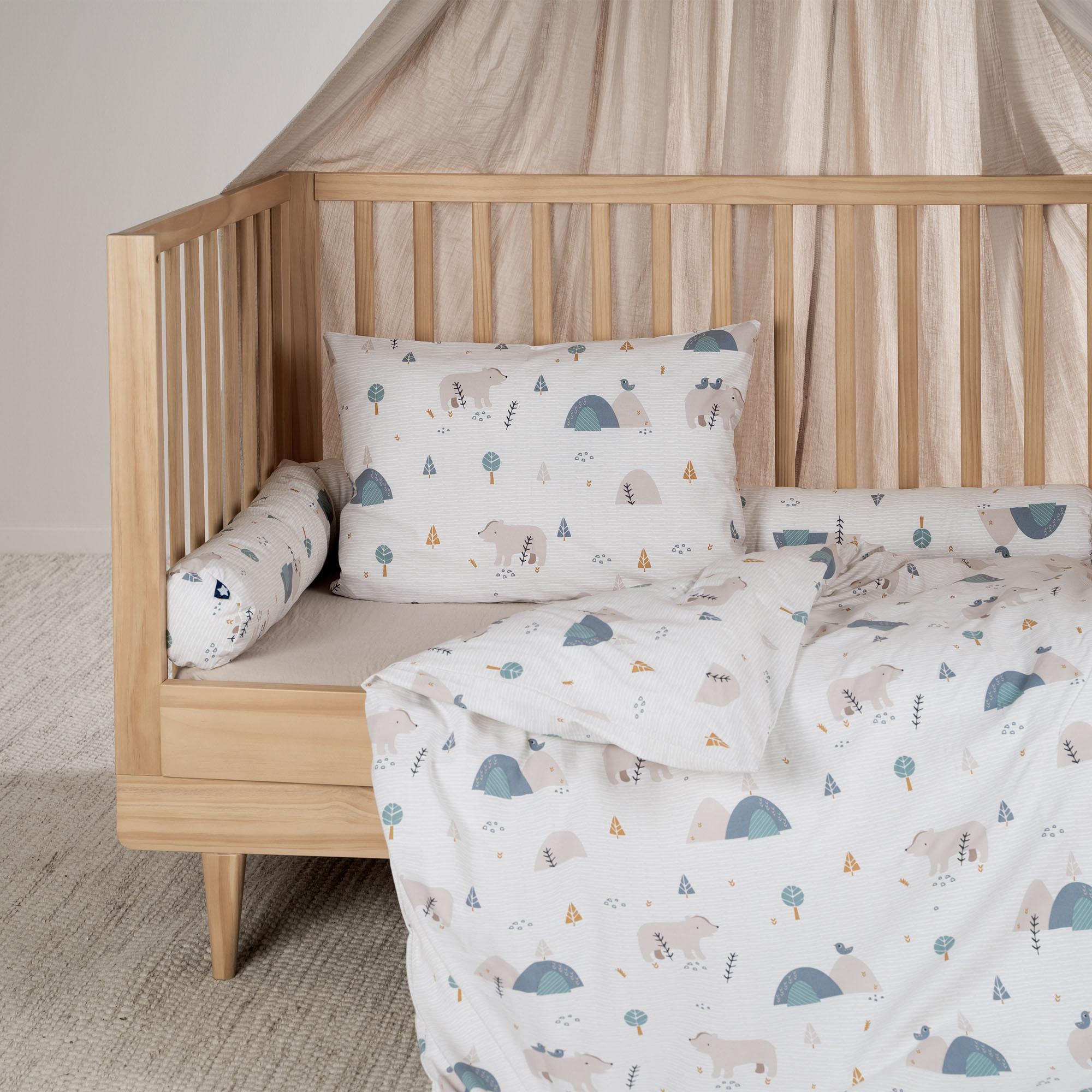 Das Bild zeigt ein Kinderbett mit aufgezogener weißer Bettwäsche mit Tier- und Naturmotiven, kombiniert mit einem passenden Kissen