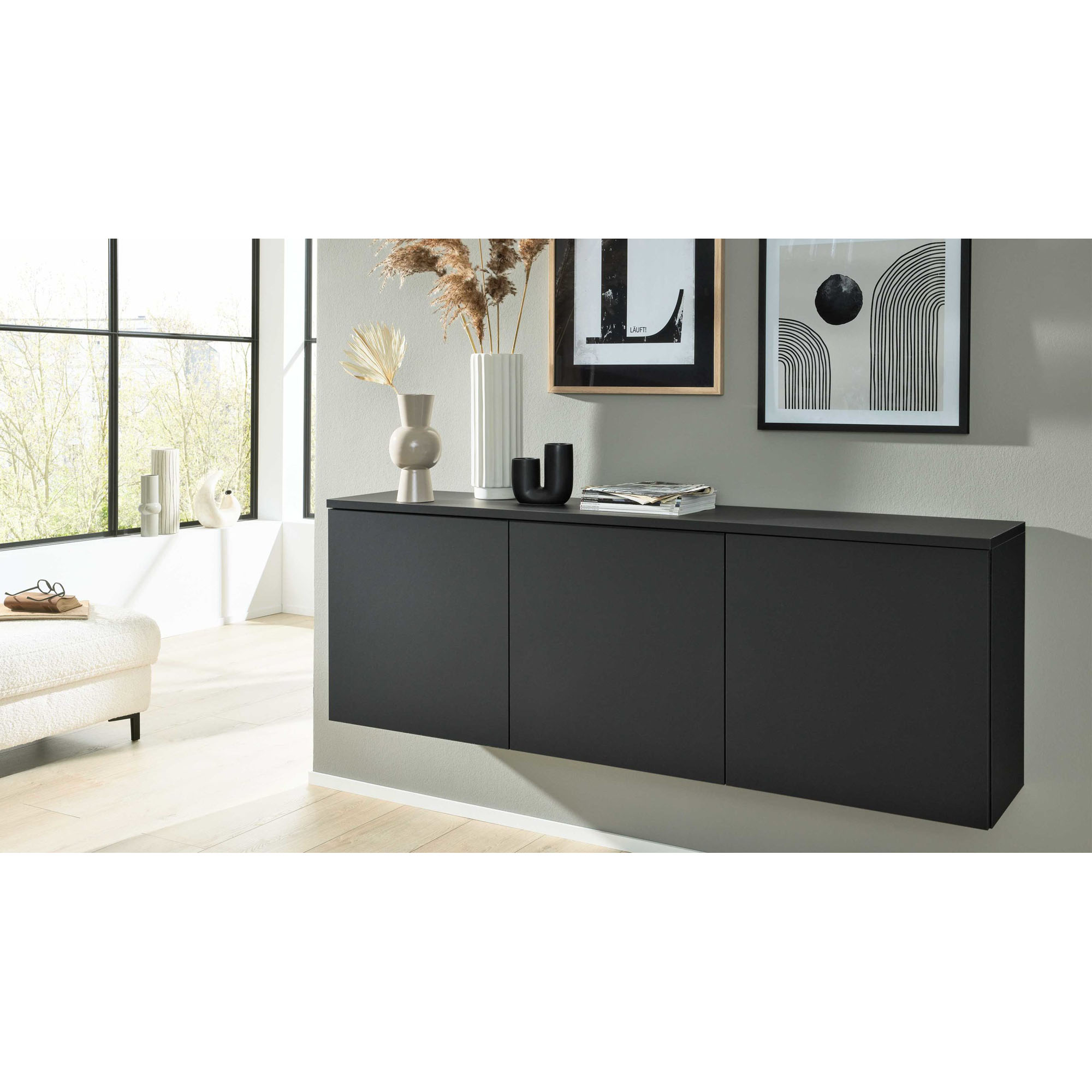 modernes dunkles Sideboard an der Wand mit dekorativen Vasen und Bildern im hellen Wohnraum