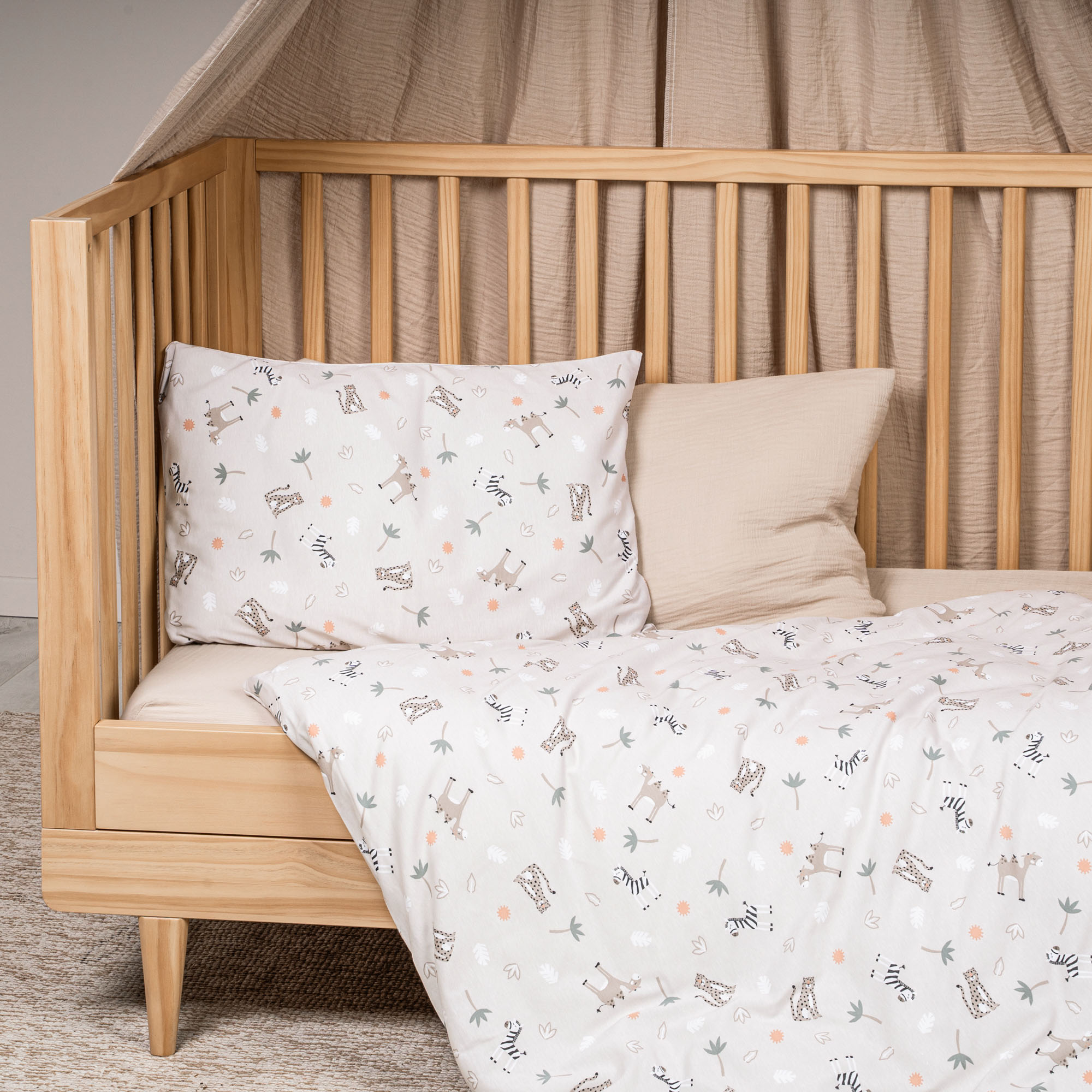 Kinderbettwäsche mit Safari-Motiven in Beige im Kinderbett dekoriert, Kopfkissen und Decke sichtbar