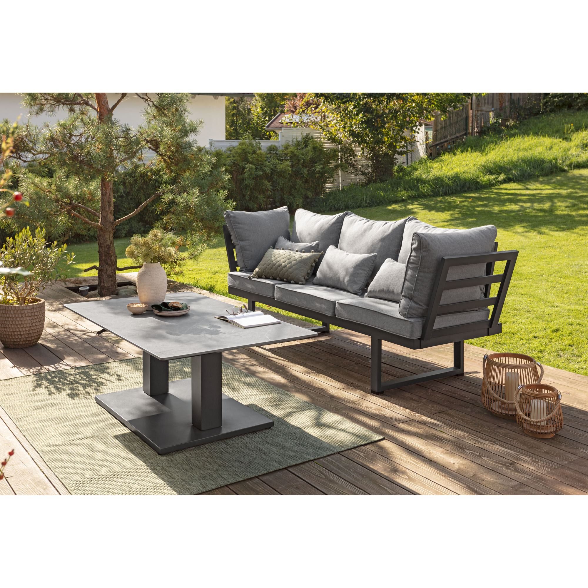 Gepolsterte Gartenbank neben einem rechteckigen Tisch auf einer Holzterrasse mit Garten und Rasen im Hintergrund