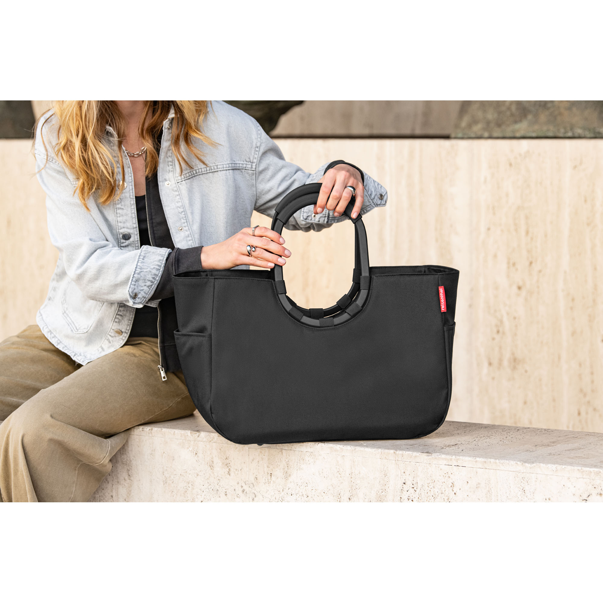 Shopper von Reisenthel, Modell Loopshopper M, in Schwarz mit schwarzen Rahmendetails, von einer Person an einem Ringgriff getragen.