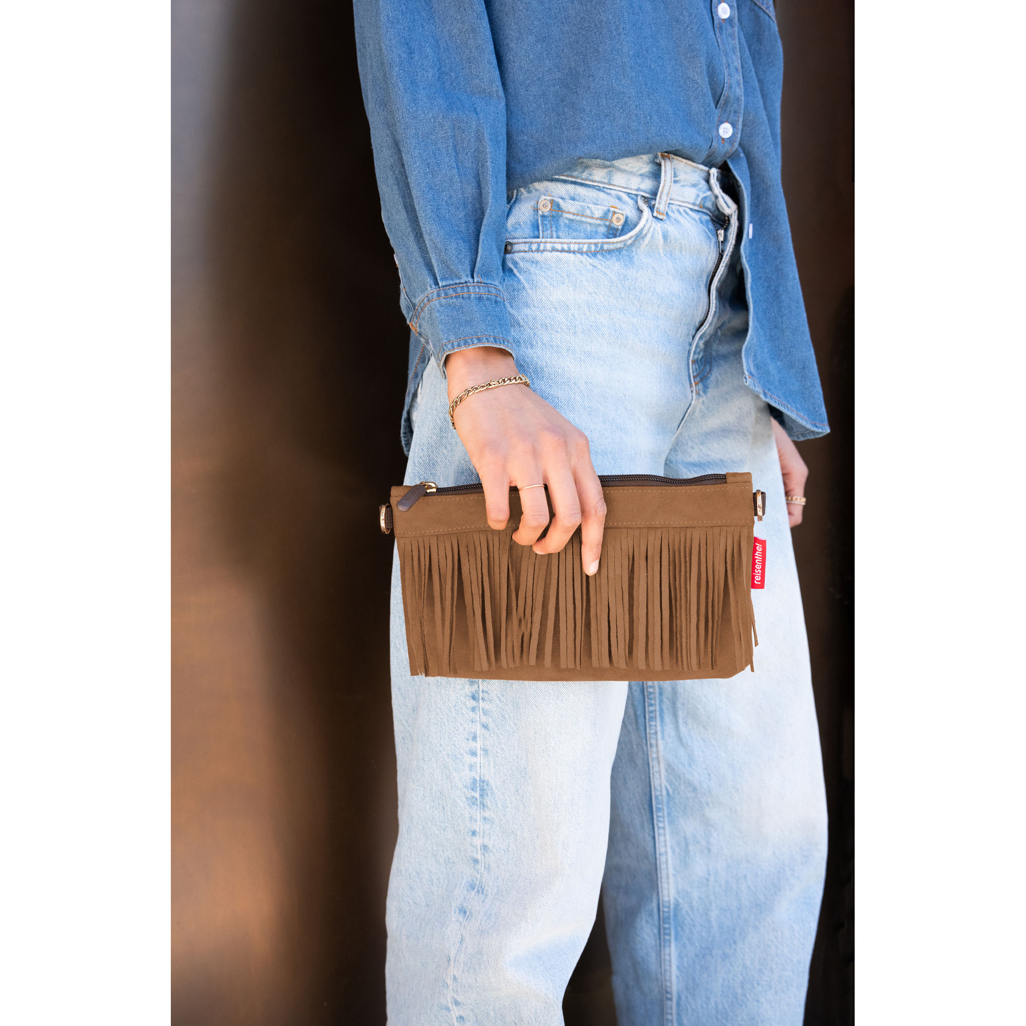 Frau hält braune Fransen-Clutch von Reisenthel in der Hand zu Jeans-Outfit