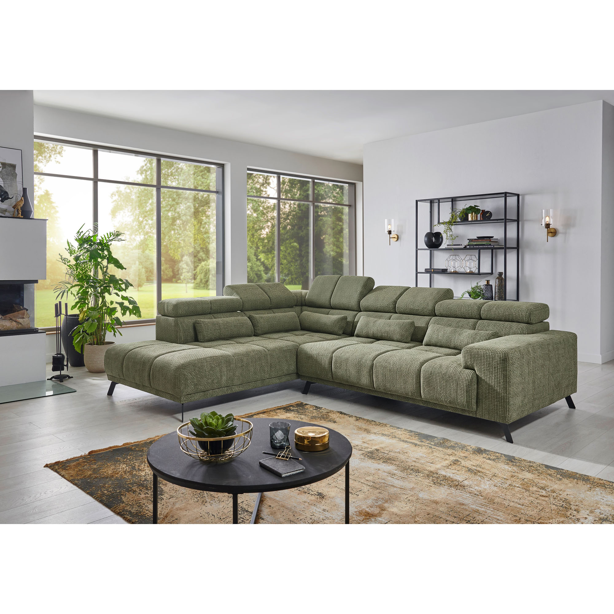 Grünes Ecksofa mit Longchair links im Bild, gepolsterten Sitzflächen, mehreren Kopfstützen und Rückenkissen in einem Wohnzimmer mit großen Fenstern
