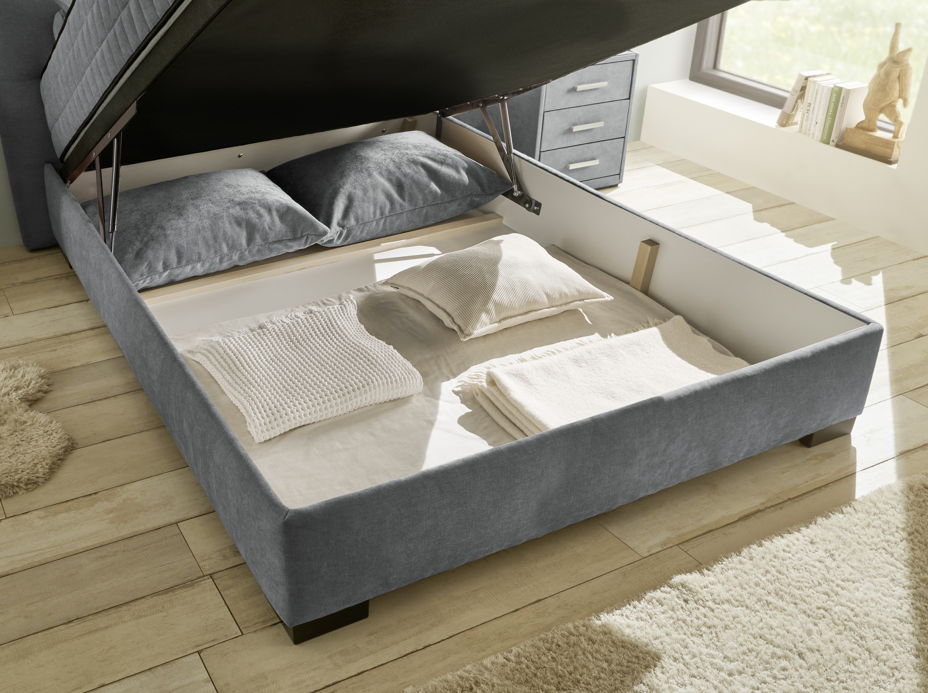 Detailaufnahme des geöffneten Bettkastens vom Boxspringbett „Wind 89 anthrazit“ in einem Schlafzimmer, Stauraum klar erkennbar