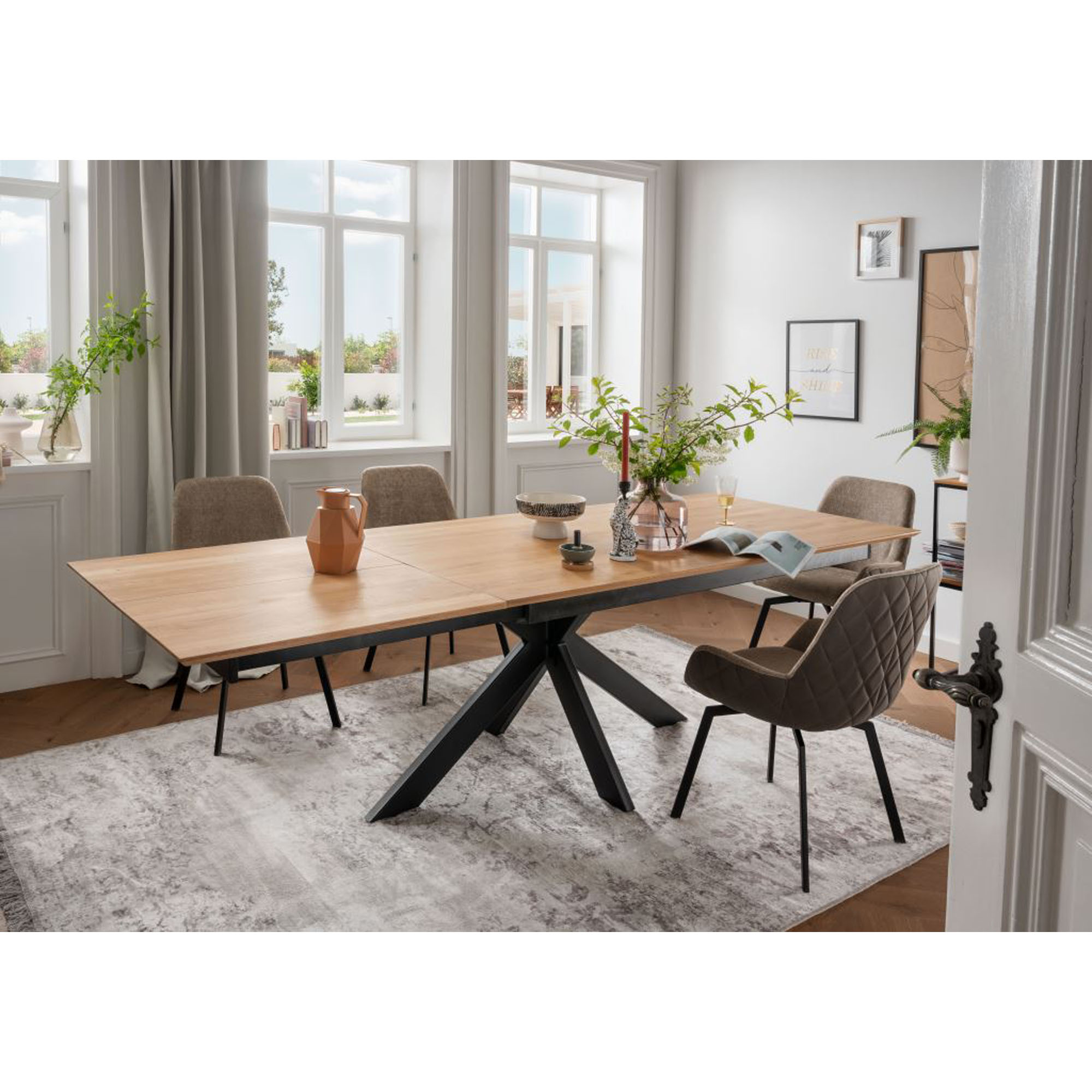 Ausziehbarer Esstisch mit Holzplatte und schwarzem Metallgestell in einem Esszimmer mit Stühlen und großen Fenstern