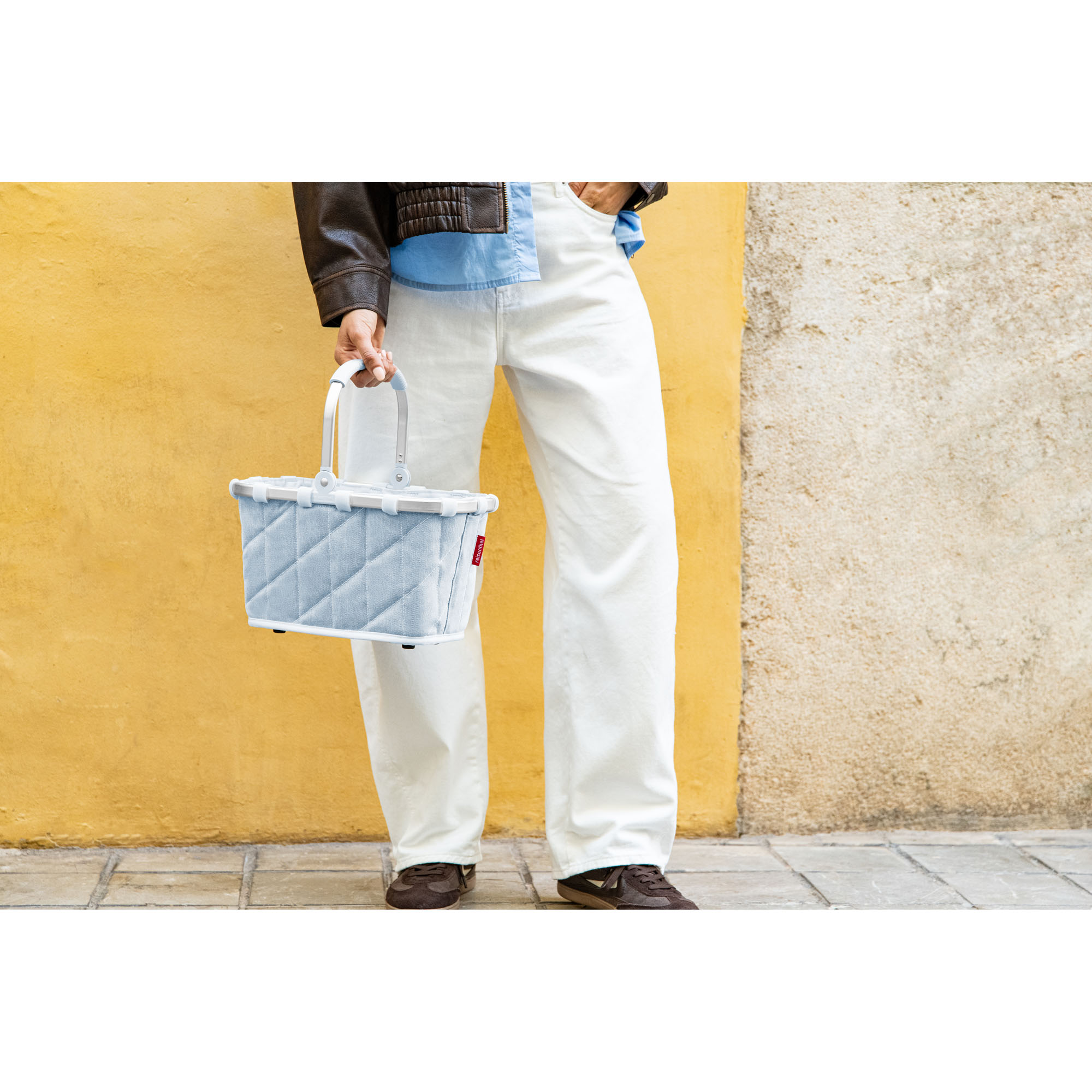 Person trägt den hellblauen Reisenthel carrybag XS in rhombus denim am Tragegriff neben dem Körper
