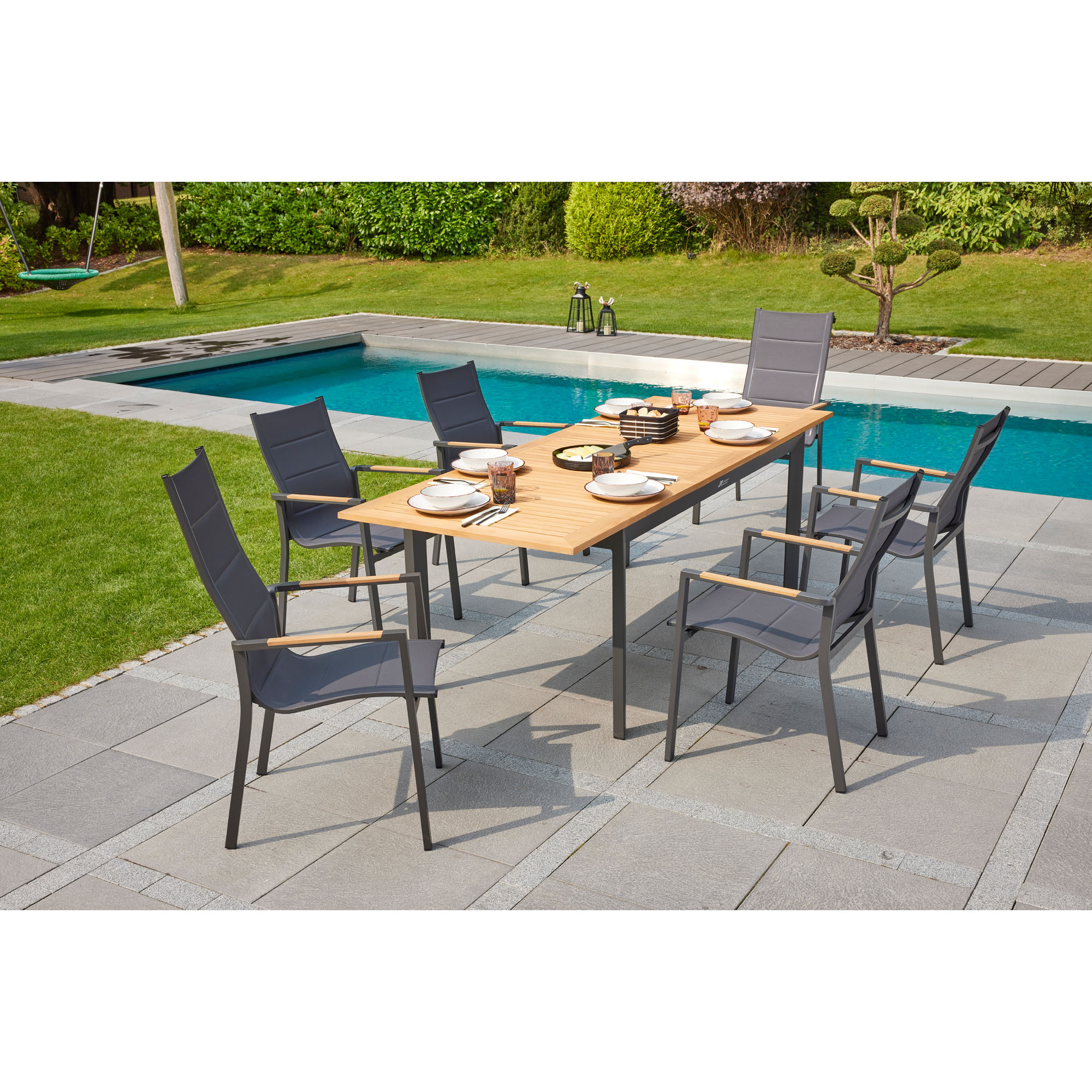 Gartentisch mit mehreren Gartenstühlen auf einer gepflasterten Terrasse neben einem Pool