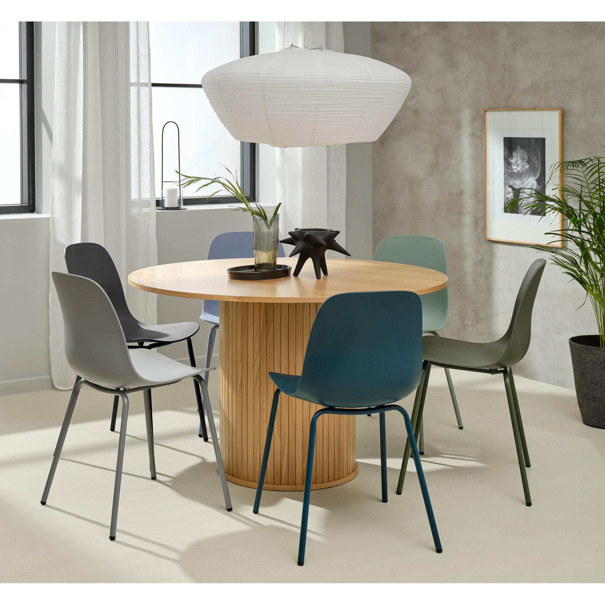 Moderner Essbereich mit rundem Holztisch und gemischten Kunststoffstühlen in Grau, Blau und Grün