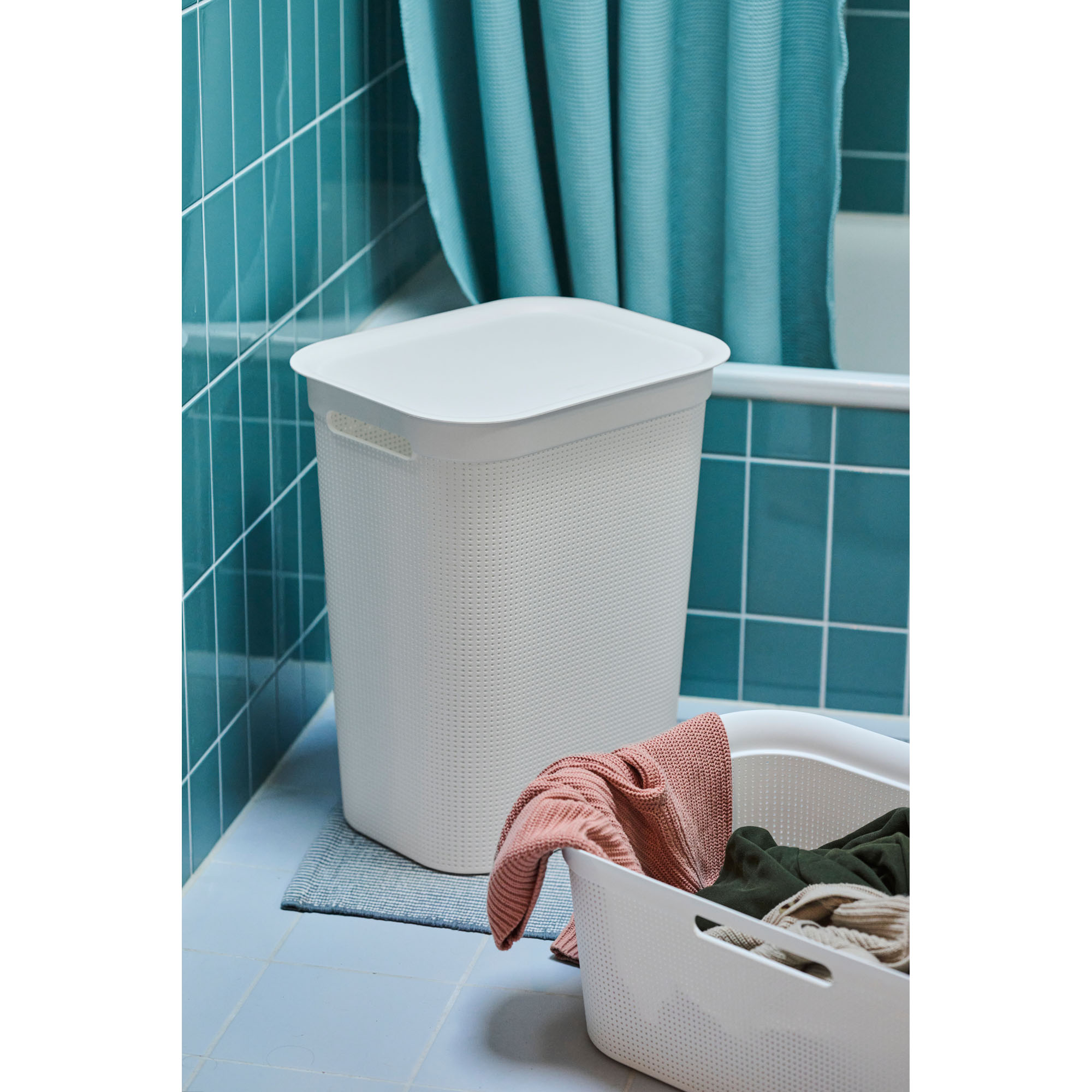 Weißer Wäschekorb mit Deckel in einem Badezimmer neben einer Badewanne