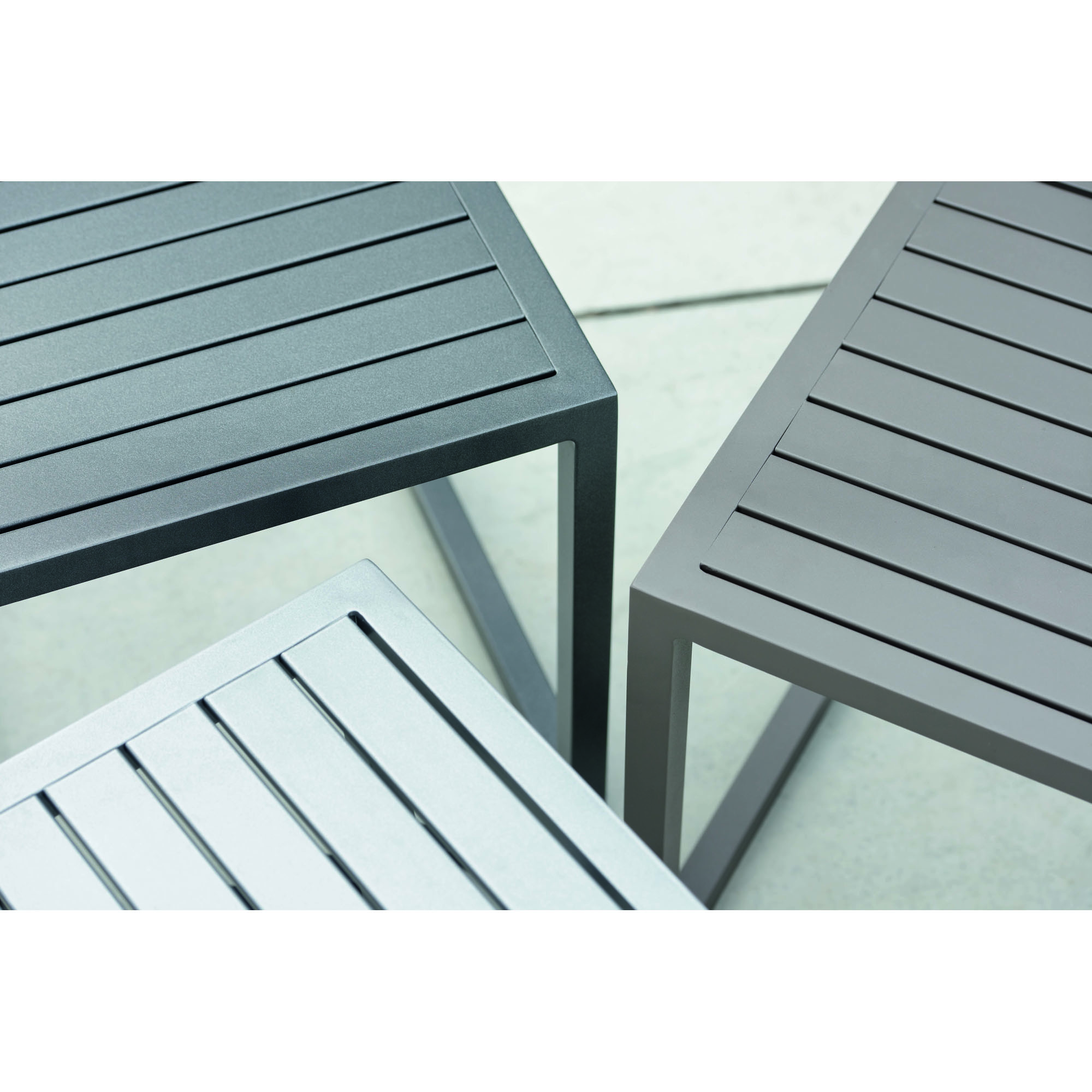 Schräg von oben aufgenommene Detailansicht von drei quadratischen Metalltischen, Fokus auf Tischplatten mit Längsrillen und rechtwinklige Ecken.
